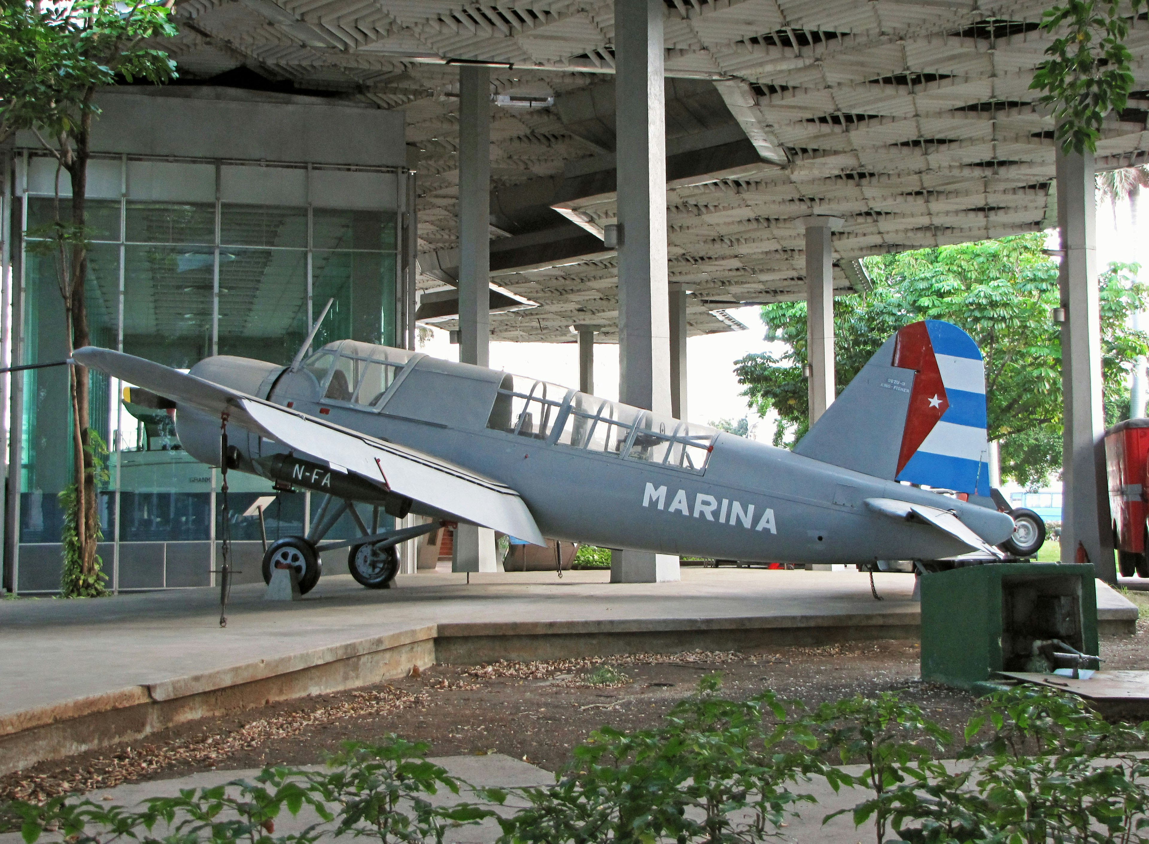 Avión militar gris expuesto al aire libre con cola roja y azul que lleva la inscripción MARINA