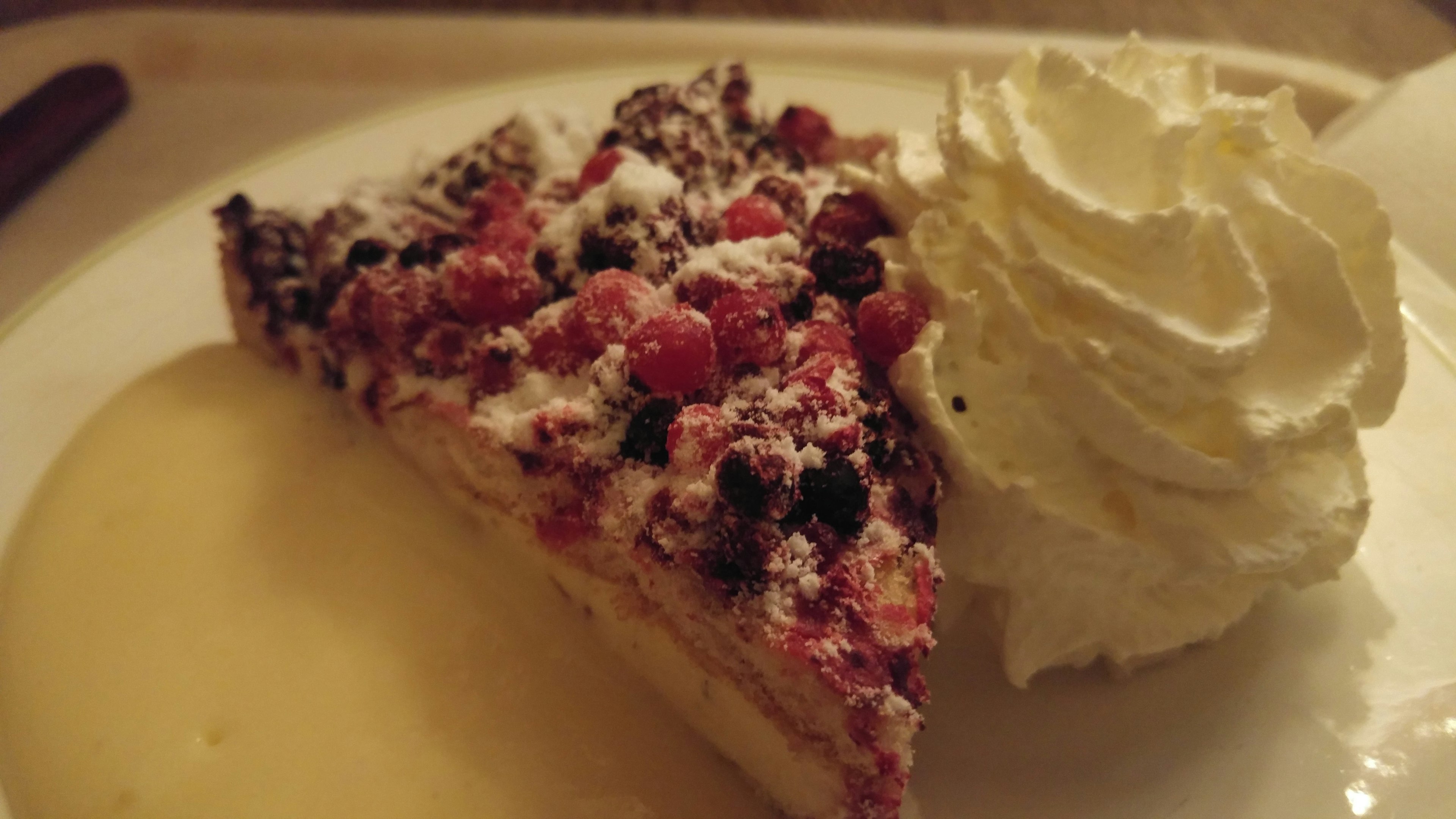 A slice of dessert topped with cream and mixed berries with a sauce