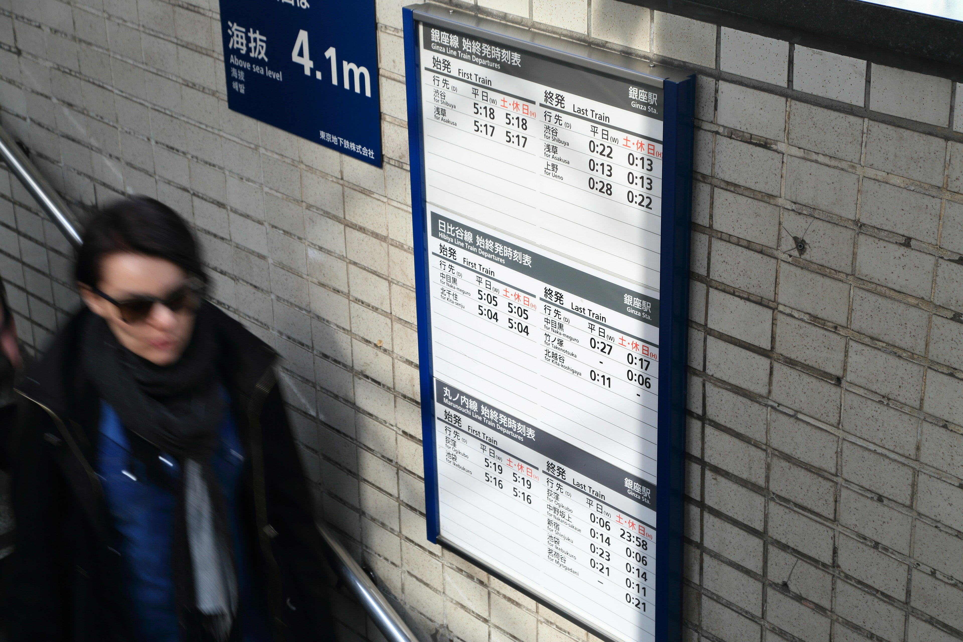 Una mujer caminando junto a un panel de horarios del metro y un letrero de 4,1 m