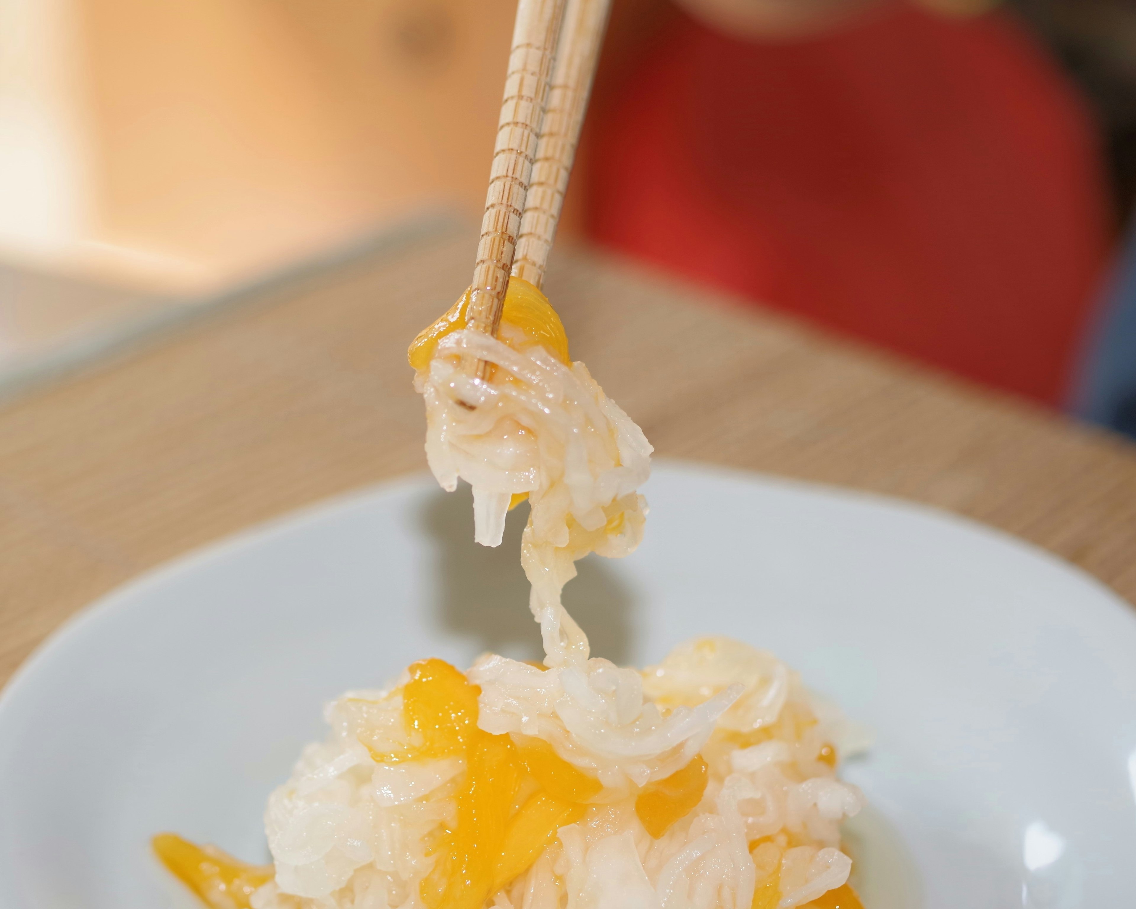 A hand lifting orange and white jelly dessert with chopsticks