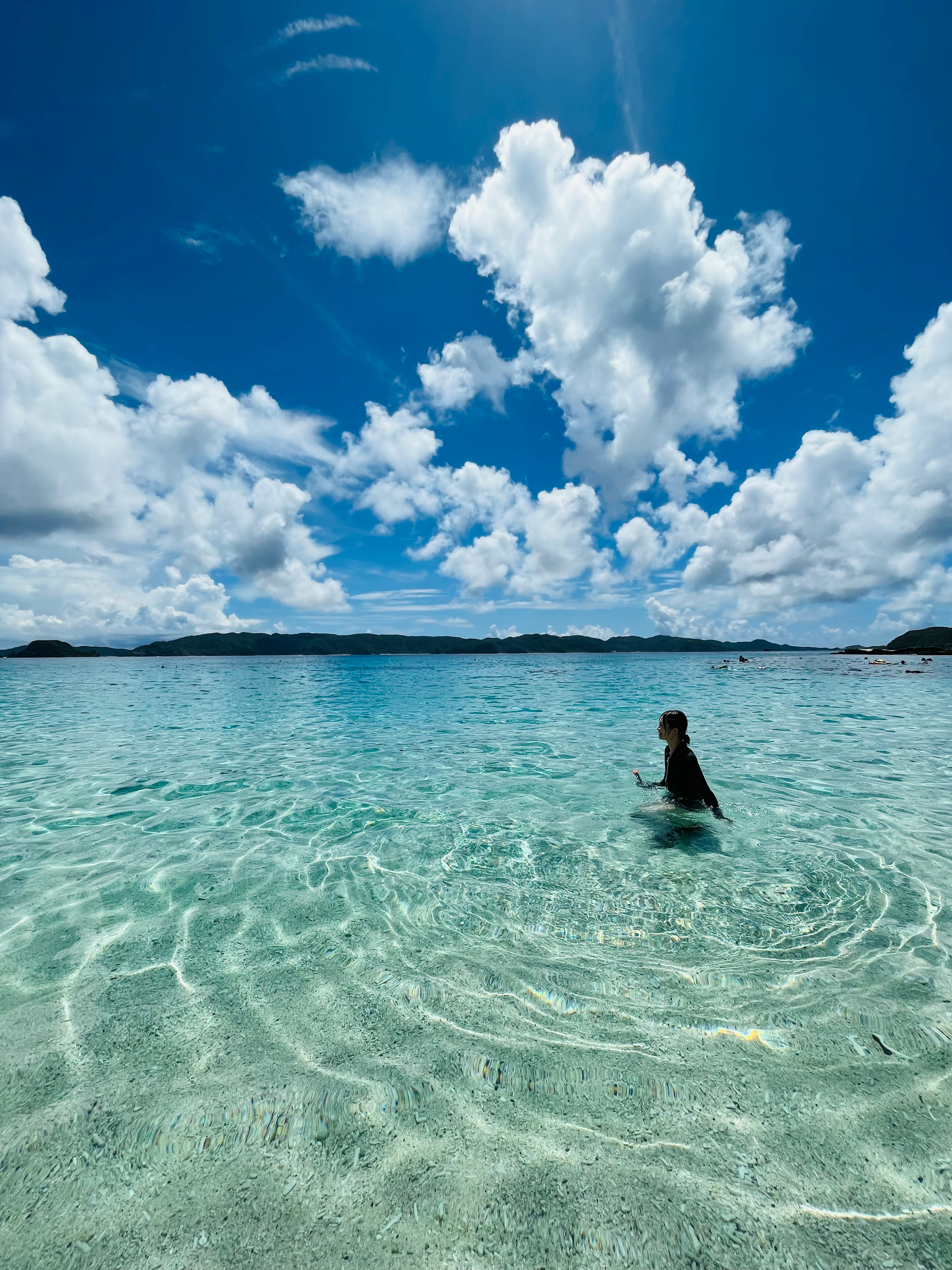 Persona nadando en agua clara bajo nubes blancas esponjosas