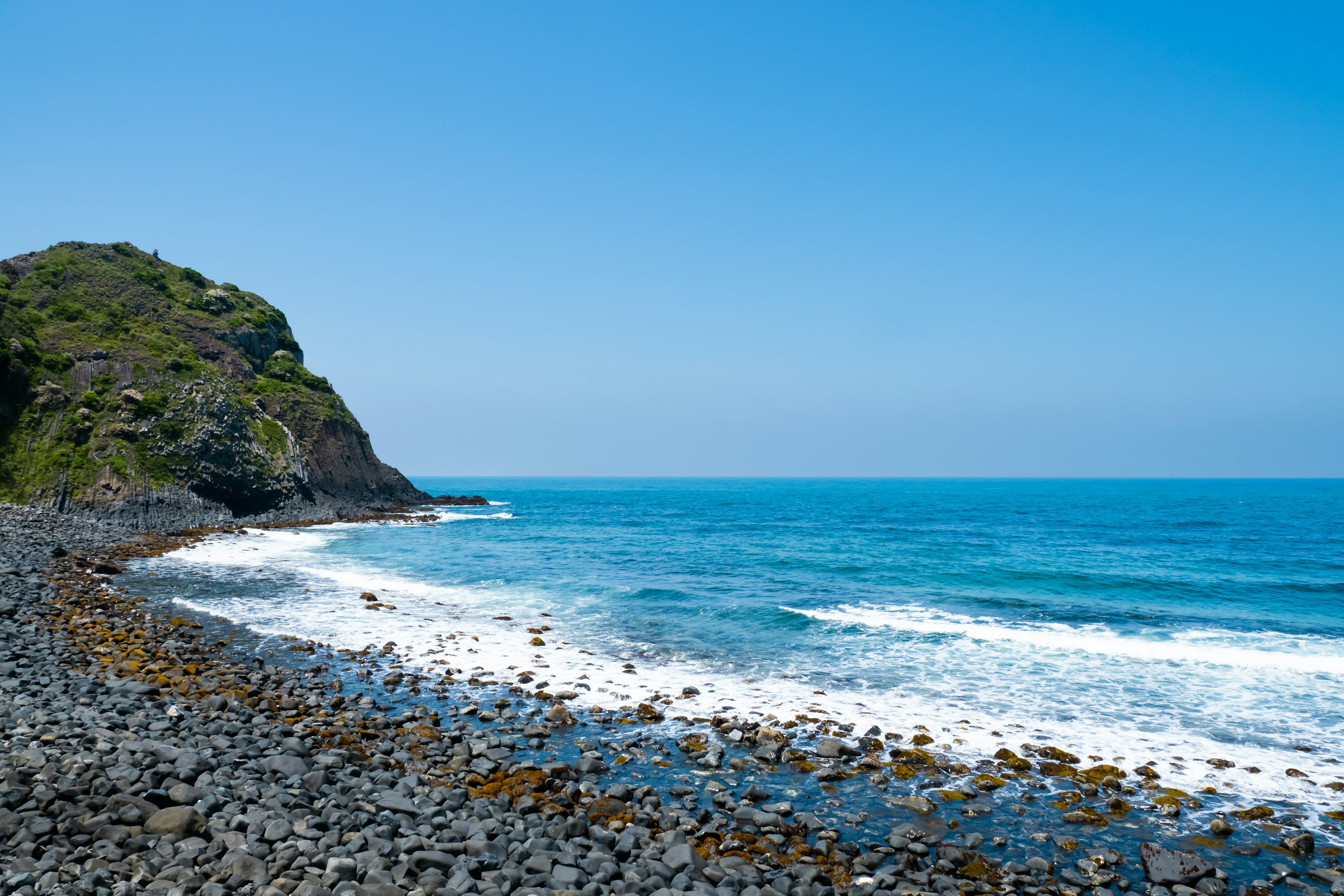 Scenic view of blue ocean with rocky shore and green hillside