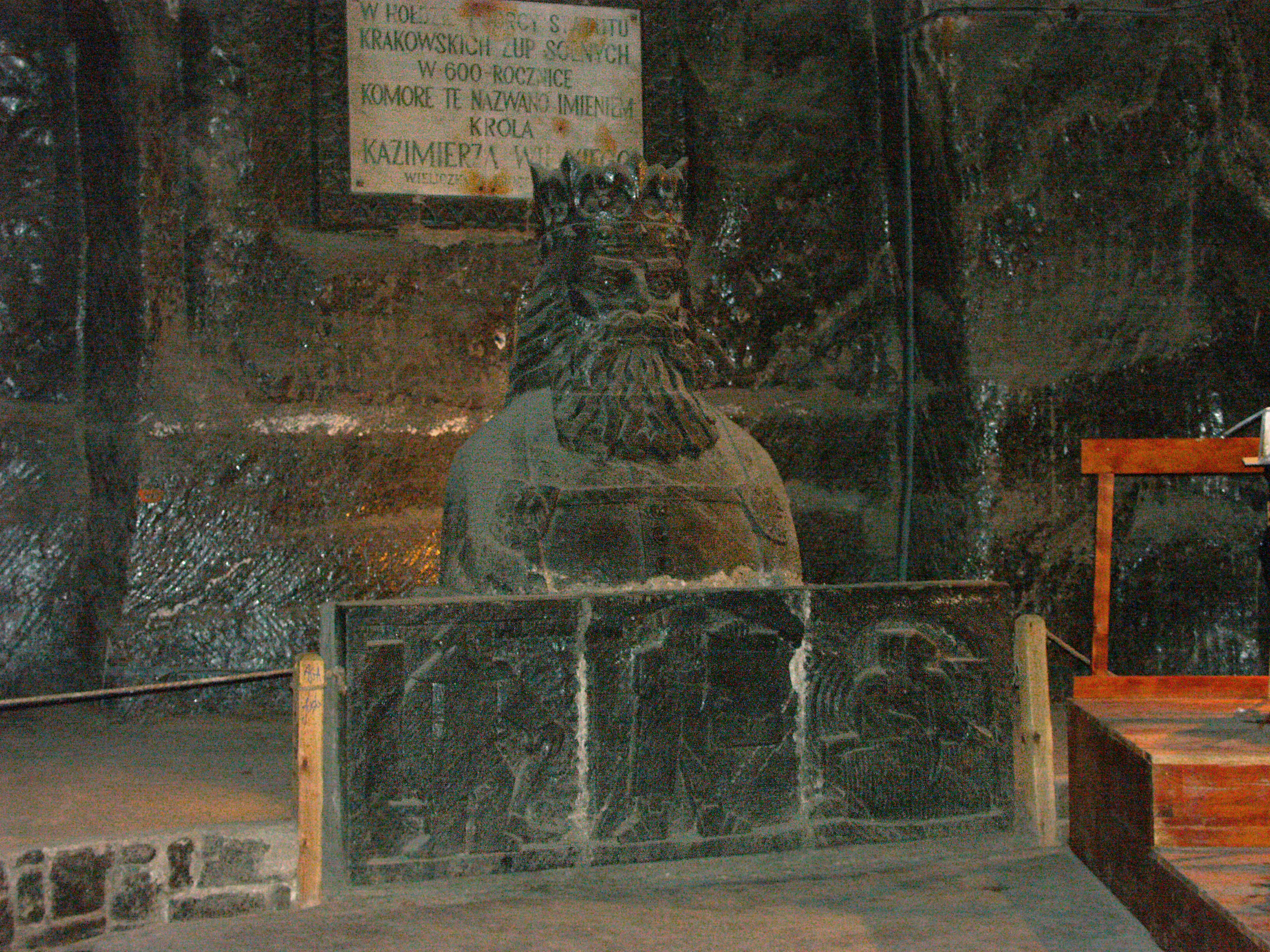 Stone statue of a king in an underground cave with rough rock walls and wooden base