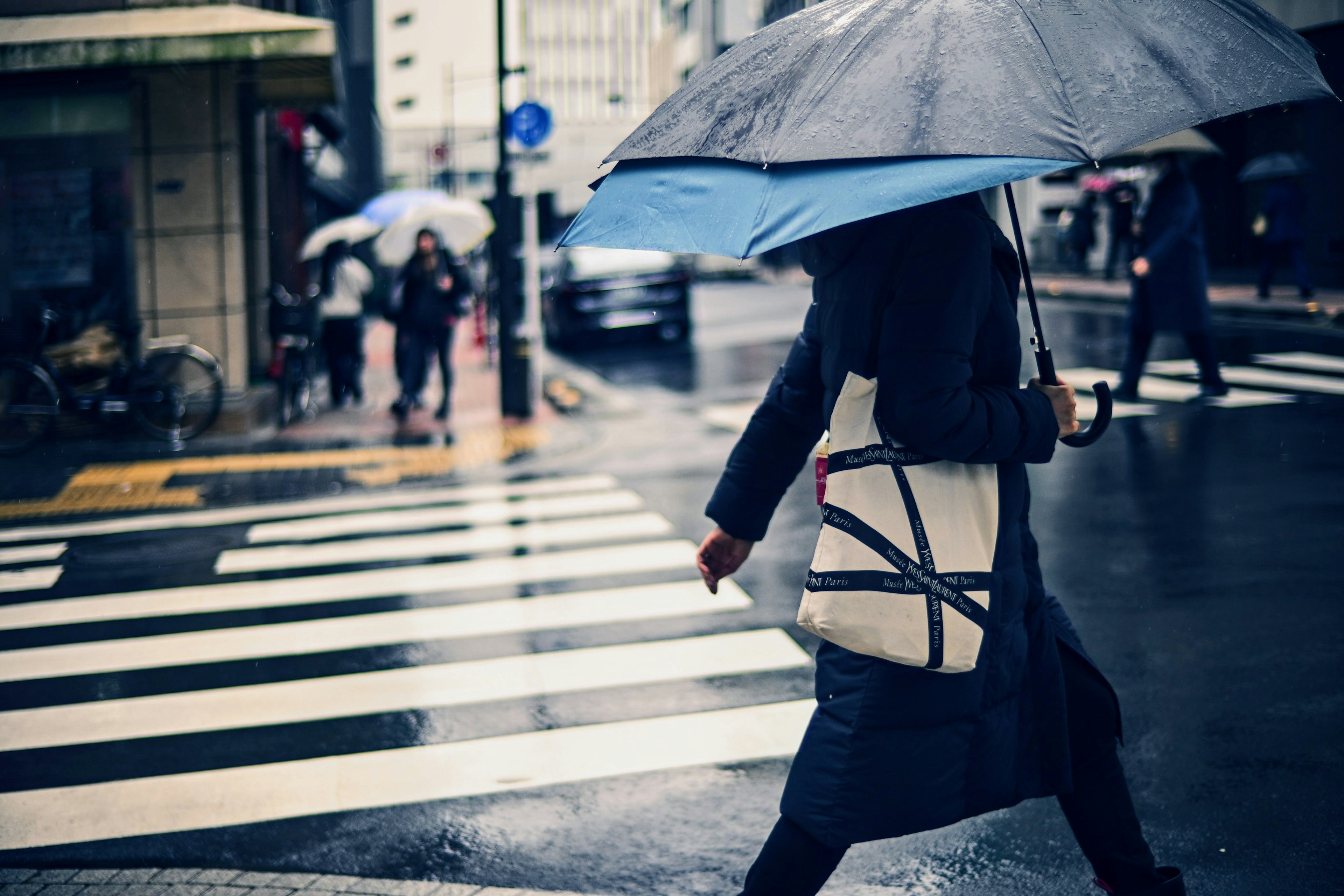 Person walking on a crosswalk with an umbrella in the rain