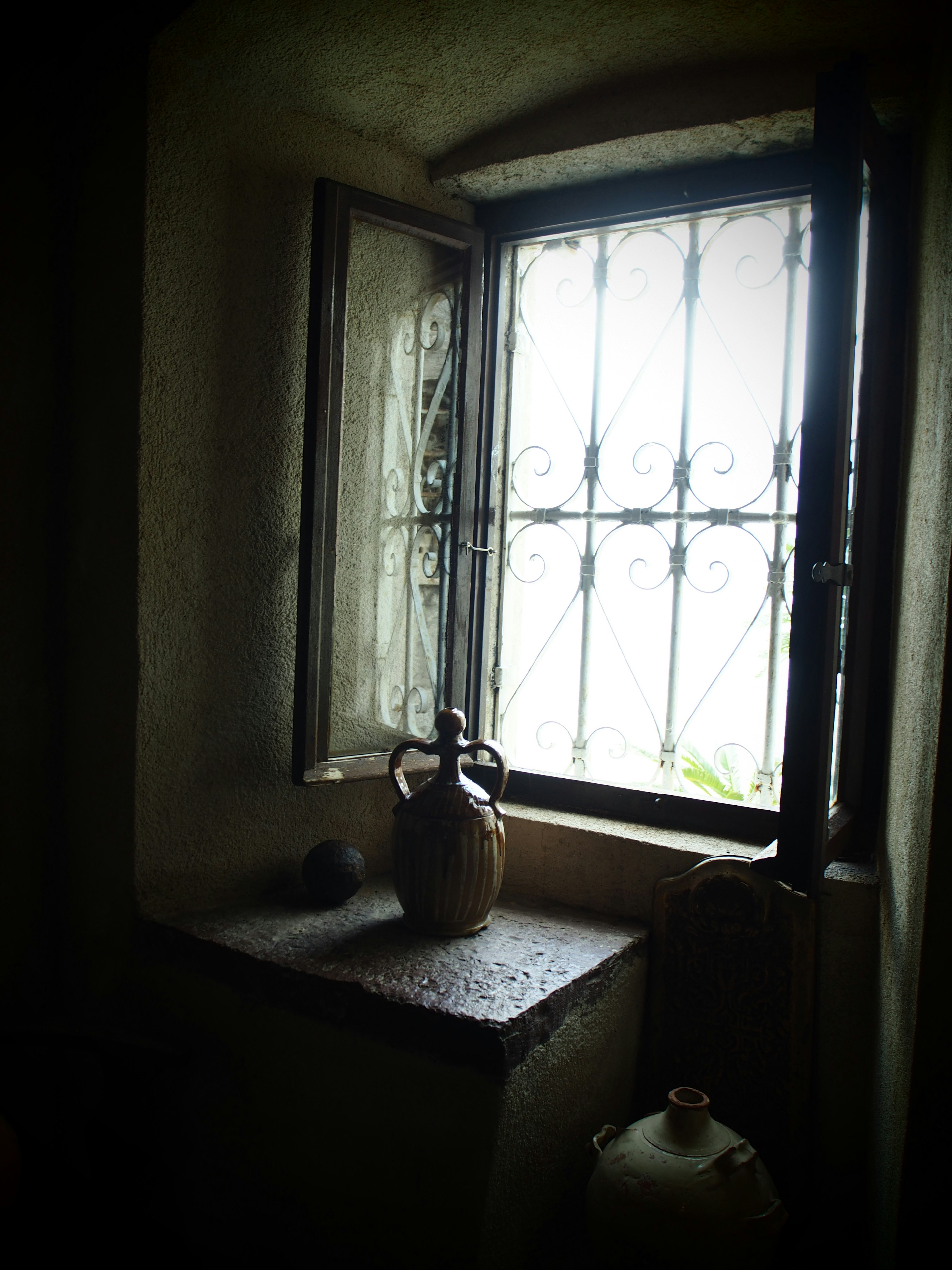 Interior de una habitación débilmente iluminada con una ventana abierta y una jarra antigua