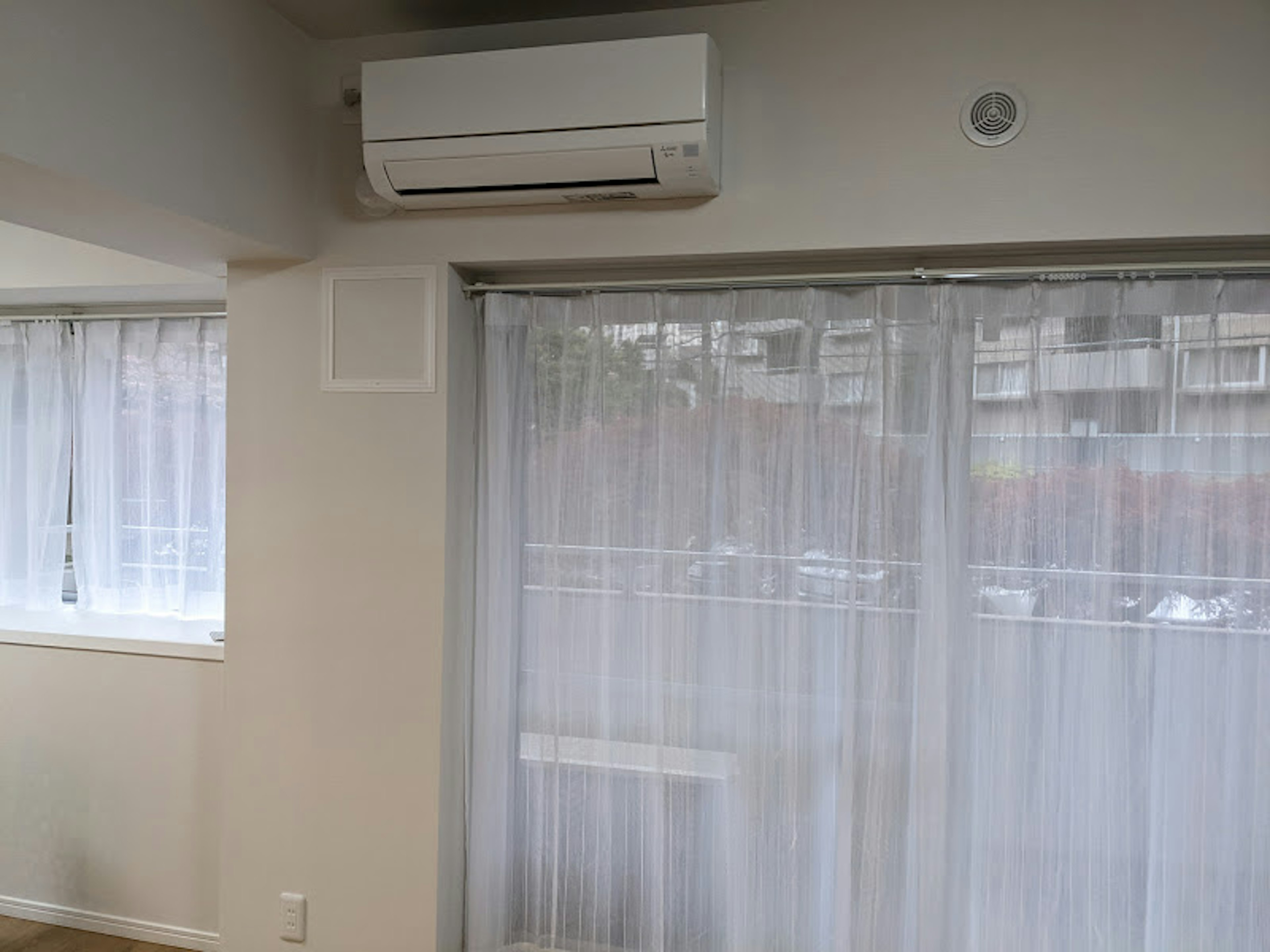 Bright corner of a room featuring an air conditioner and sheer white curtains