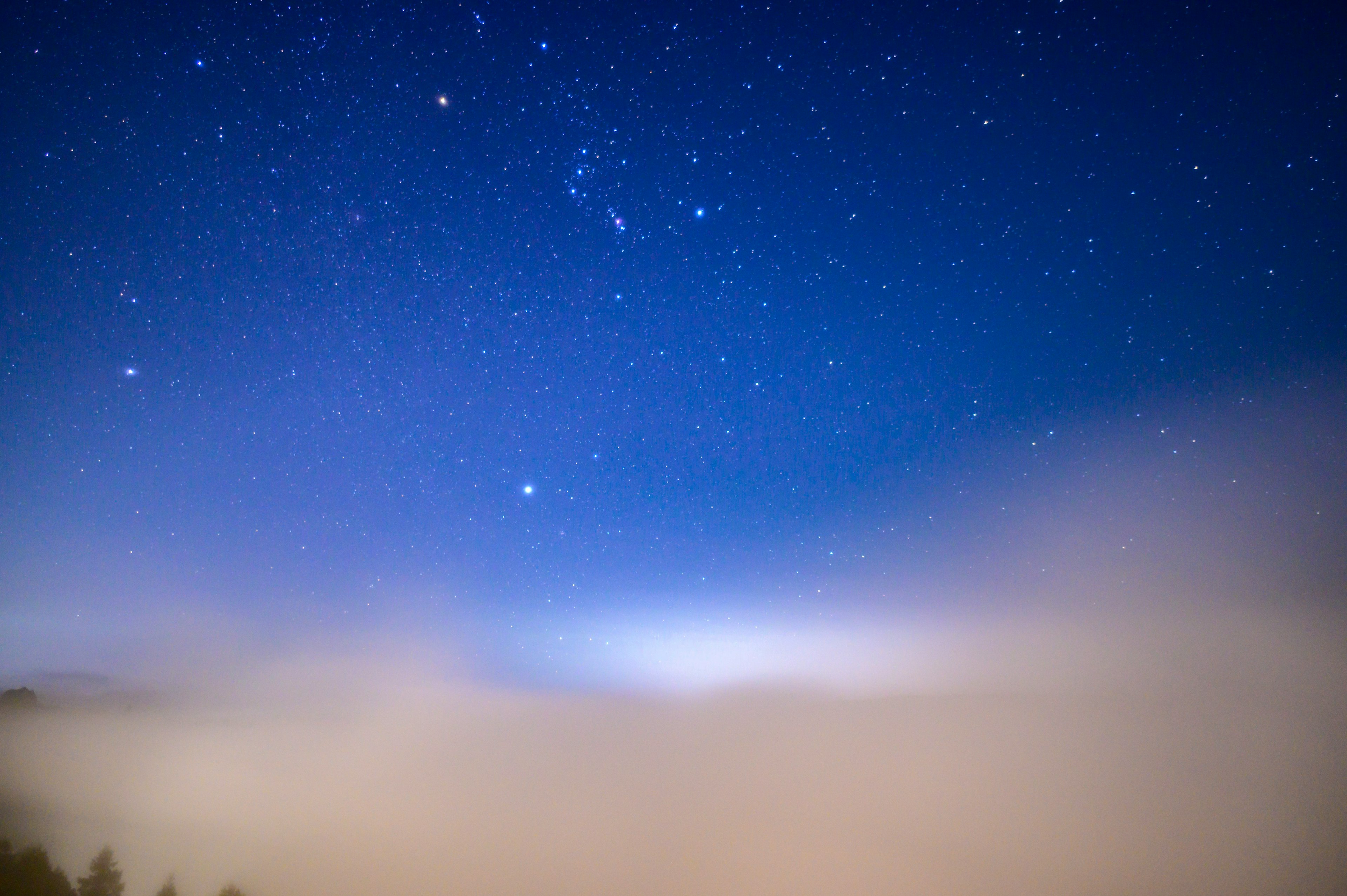 A beautiful scene with stars shining in a blue night sky above a sea of clouds