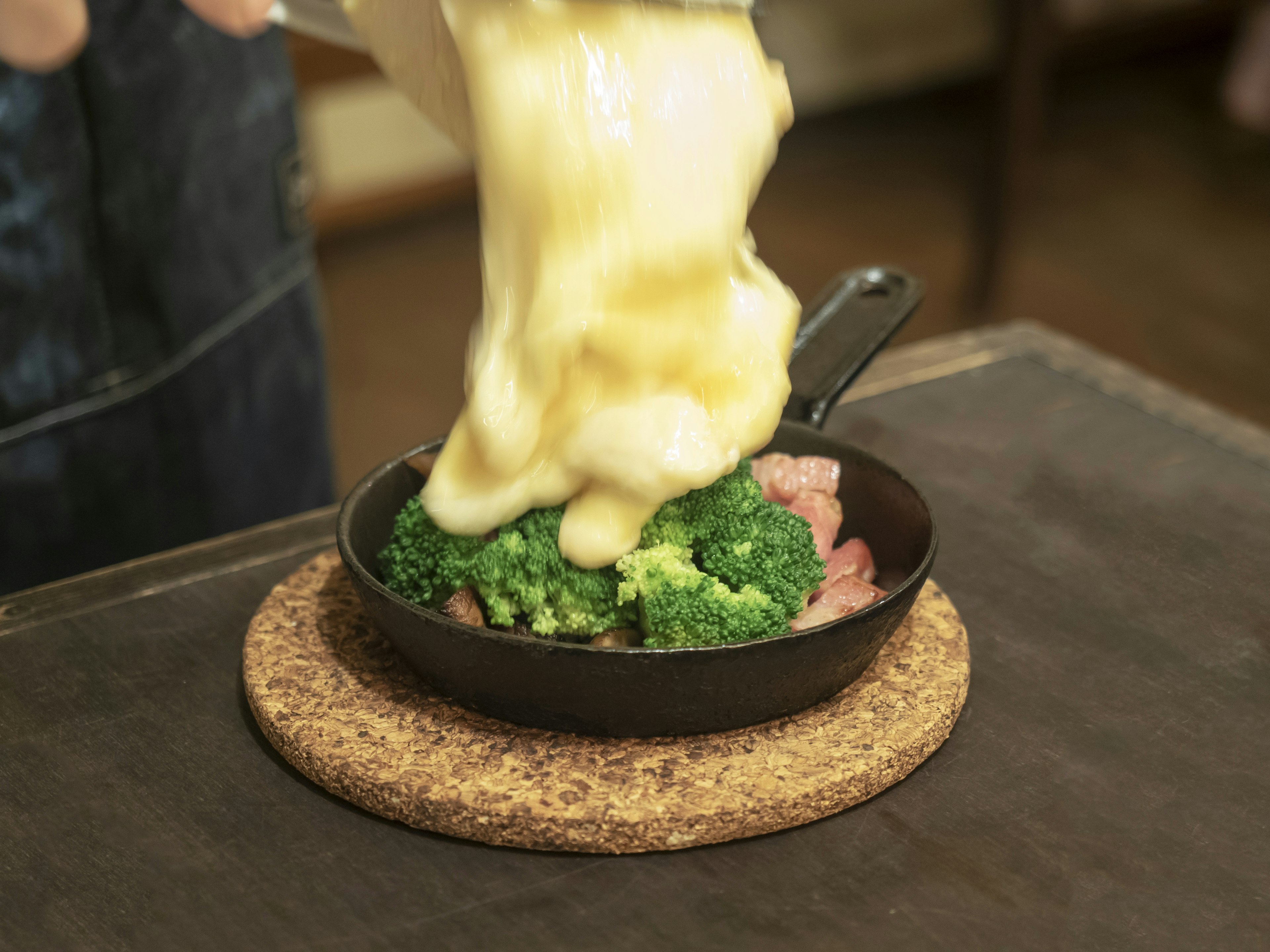 Melted cheese being poured over broccoli and meat in a skillet