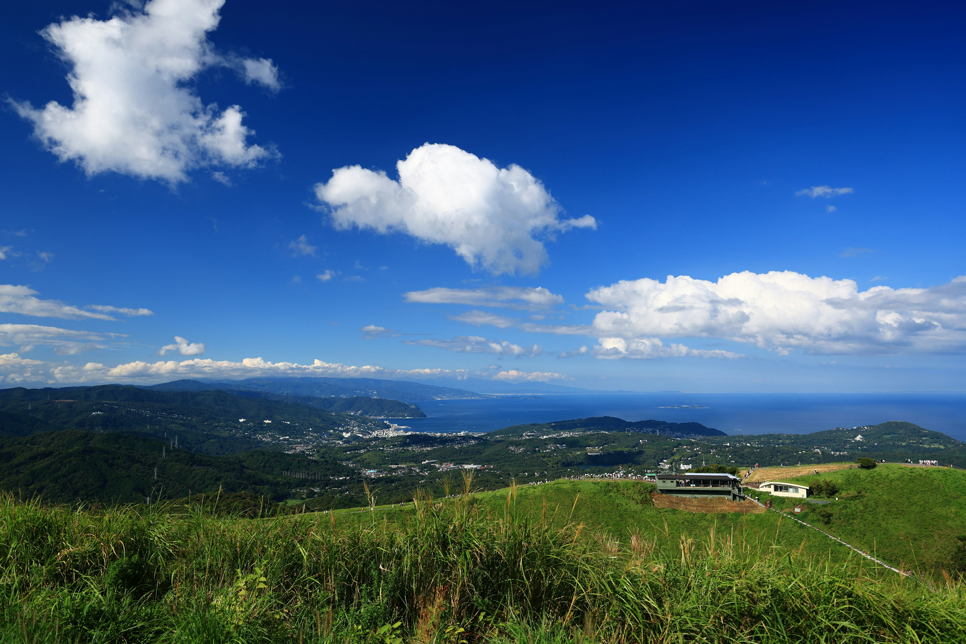 Vista panoramica di colline verdi sotto un cielo blu con nuvole bianche e oceano