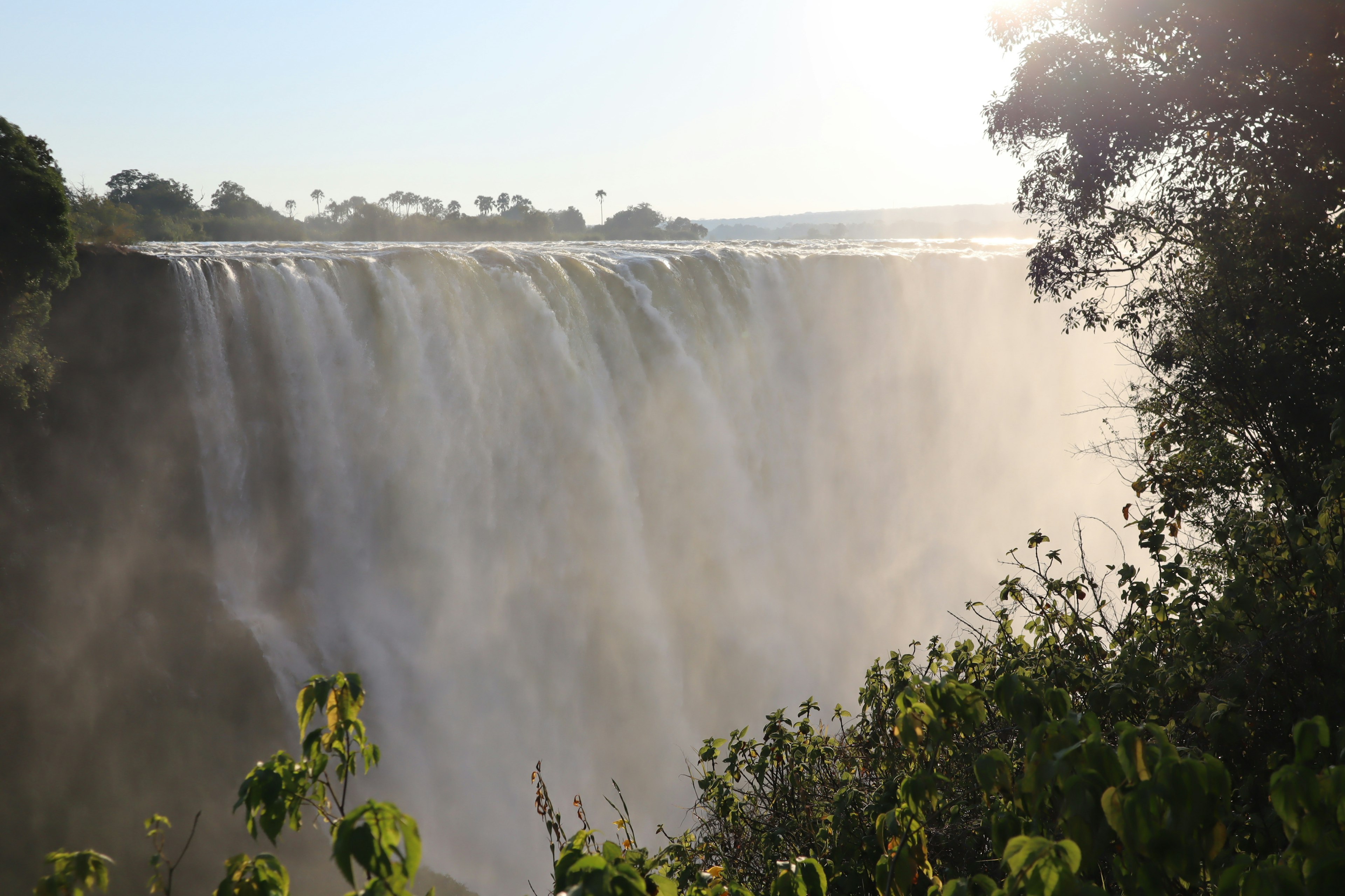 Vista maestosa della cascata con nebbia che sale fogliame verde e luce solare brillante