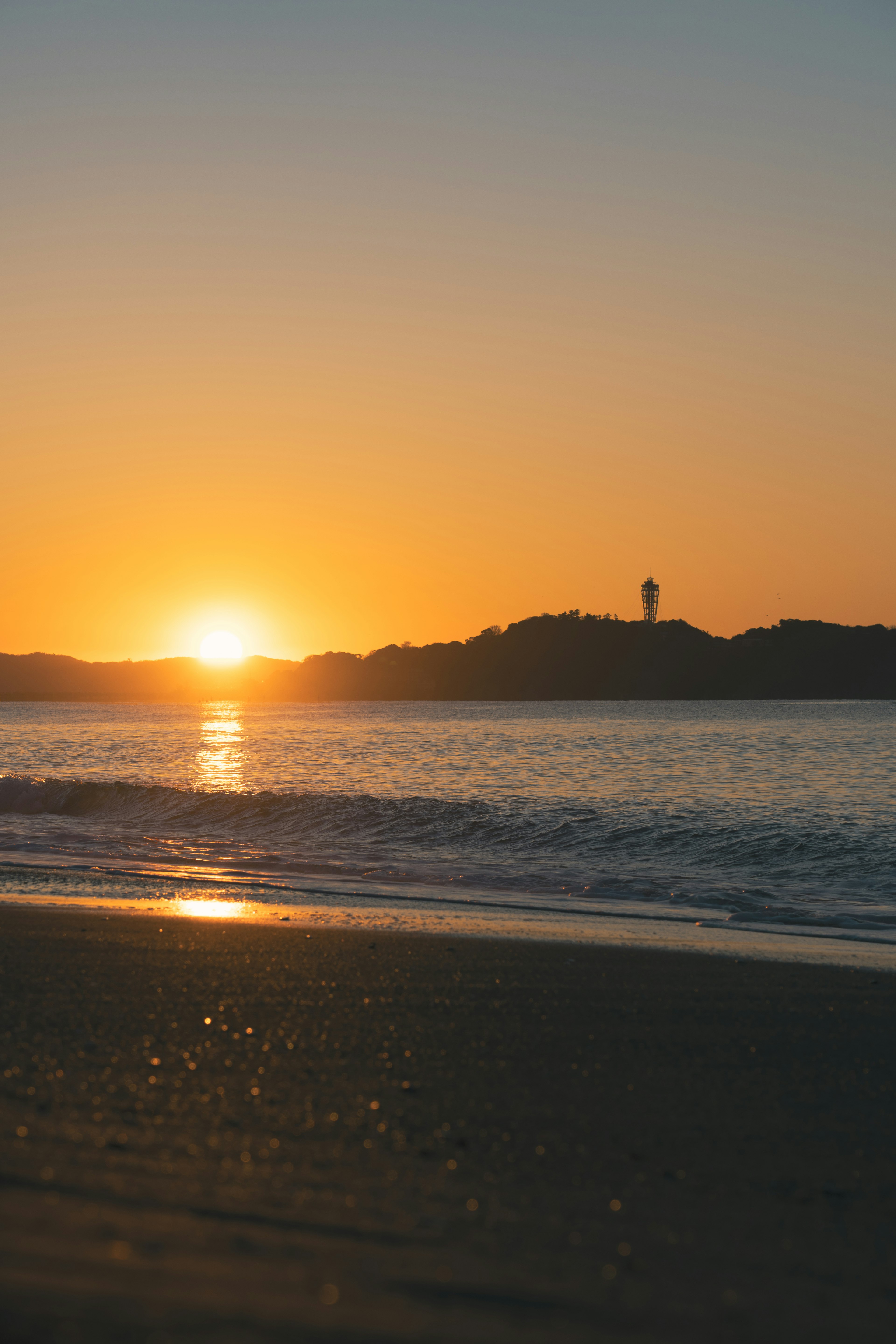 美麗的海上日落 海灘沙子和波浪的倒影 照亮的山丘輪廓