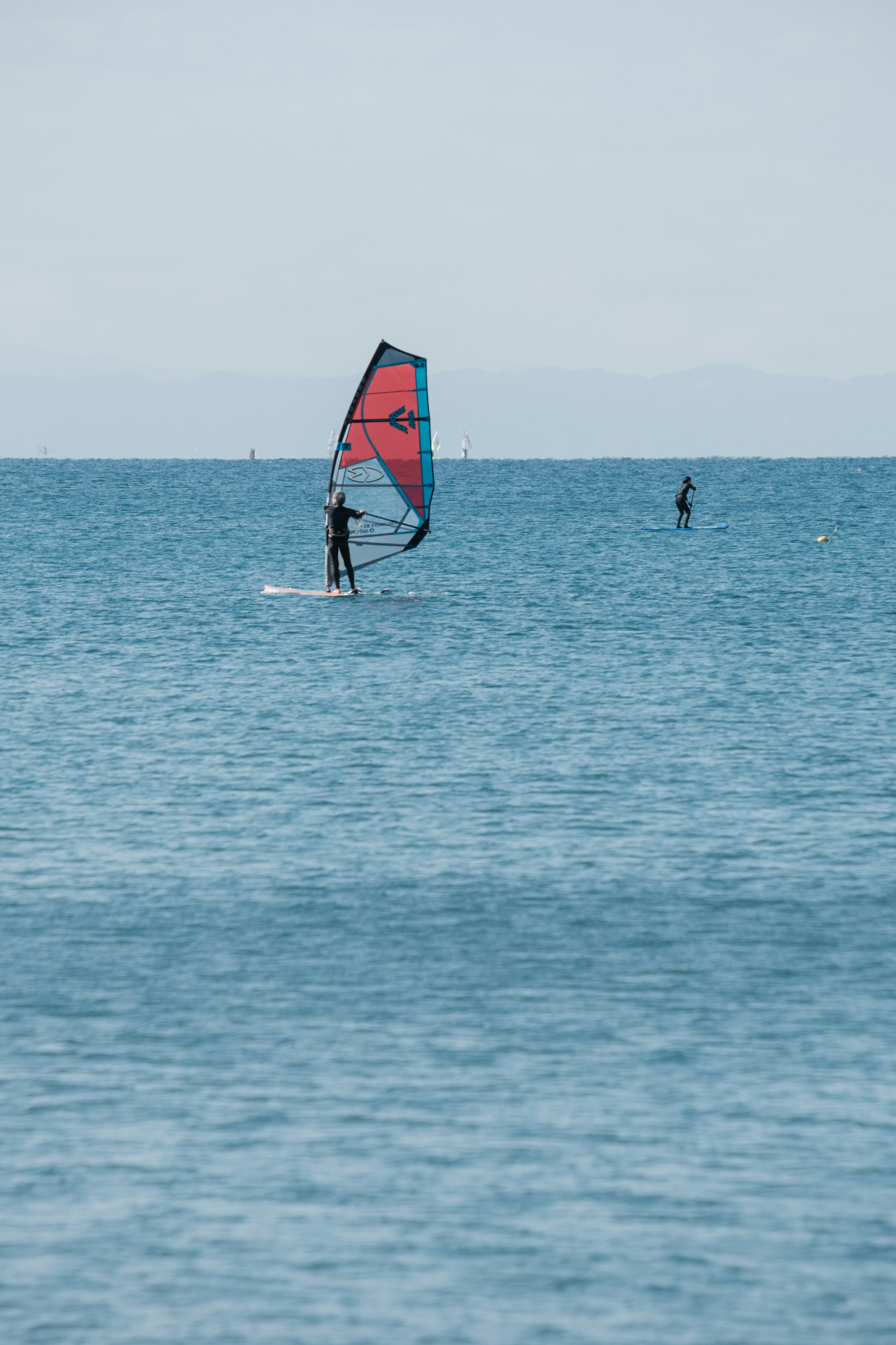 Eine Person, die auf einem blauen Meer Windsurfen genießt, mit einem anderen Surfer in der Ferne