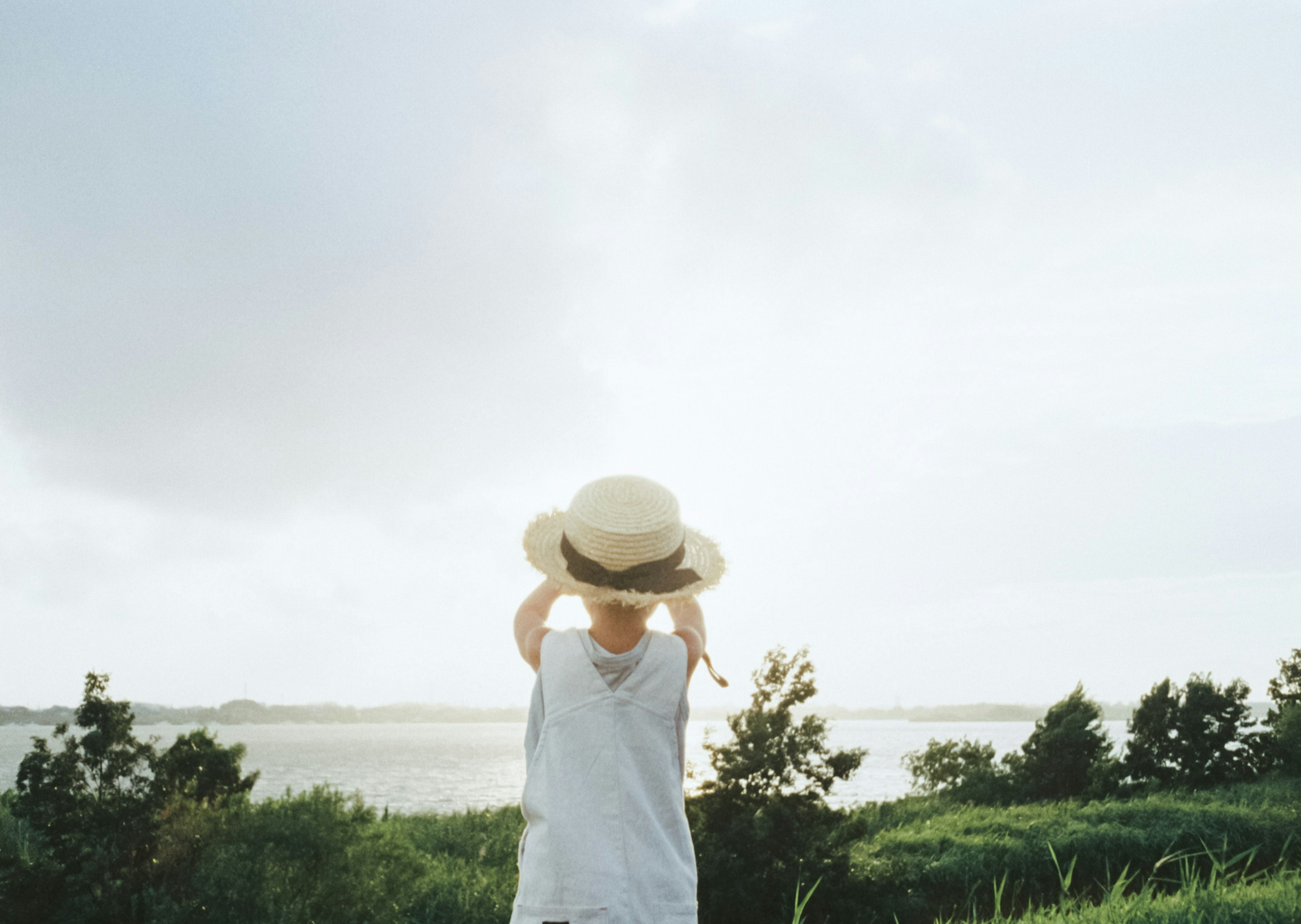 子供が帽子を持って海を見つめている風景