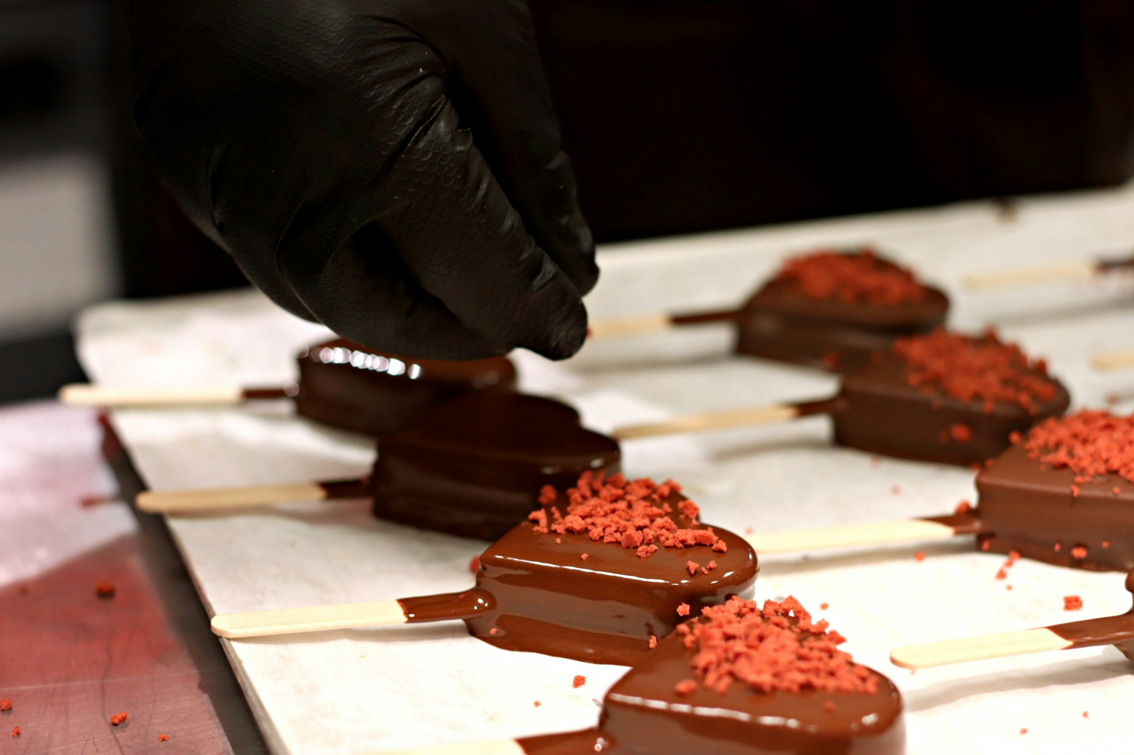 Mano agregando chispas rojas a helados en forma de corazón cubiertos de chocolate