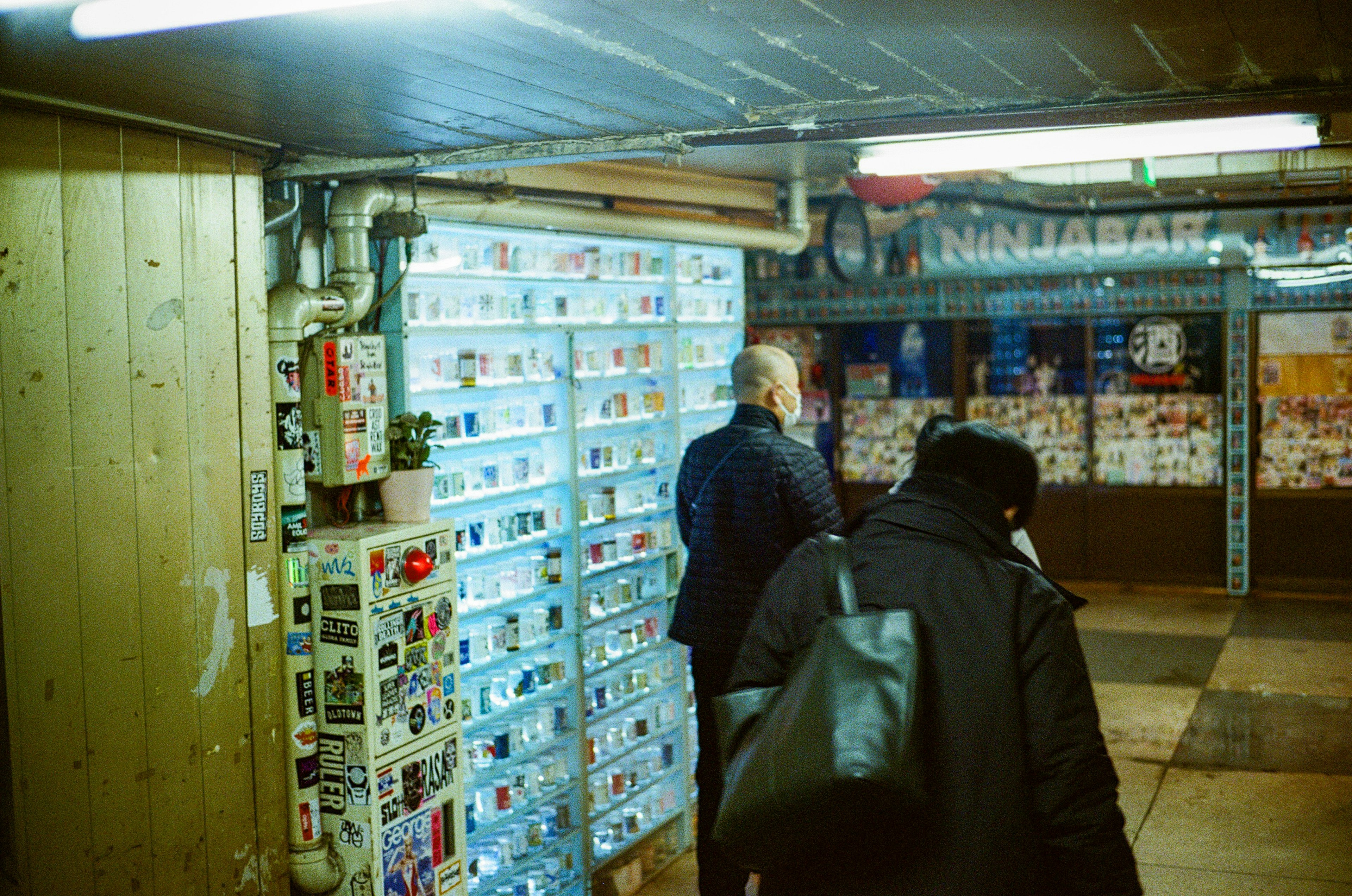 People walking past a wall of blue boxes in an underground shop