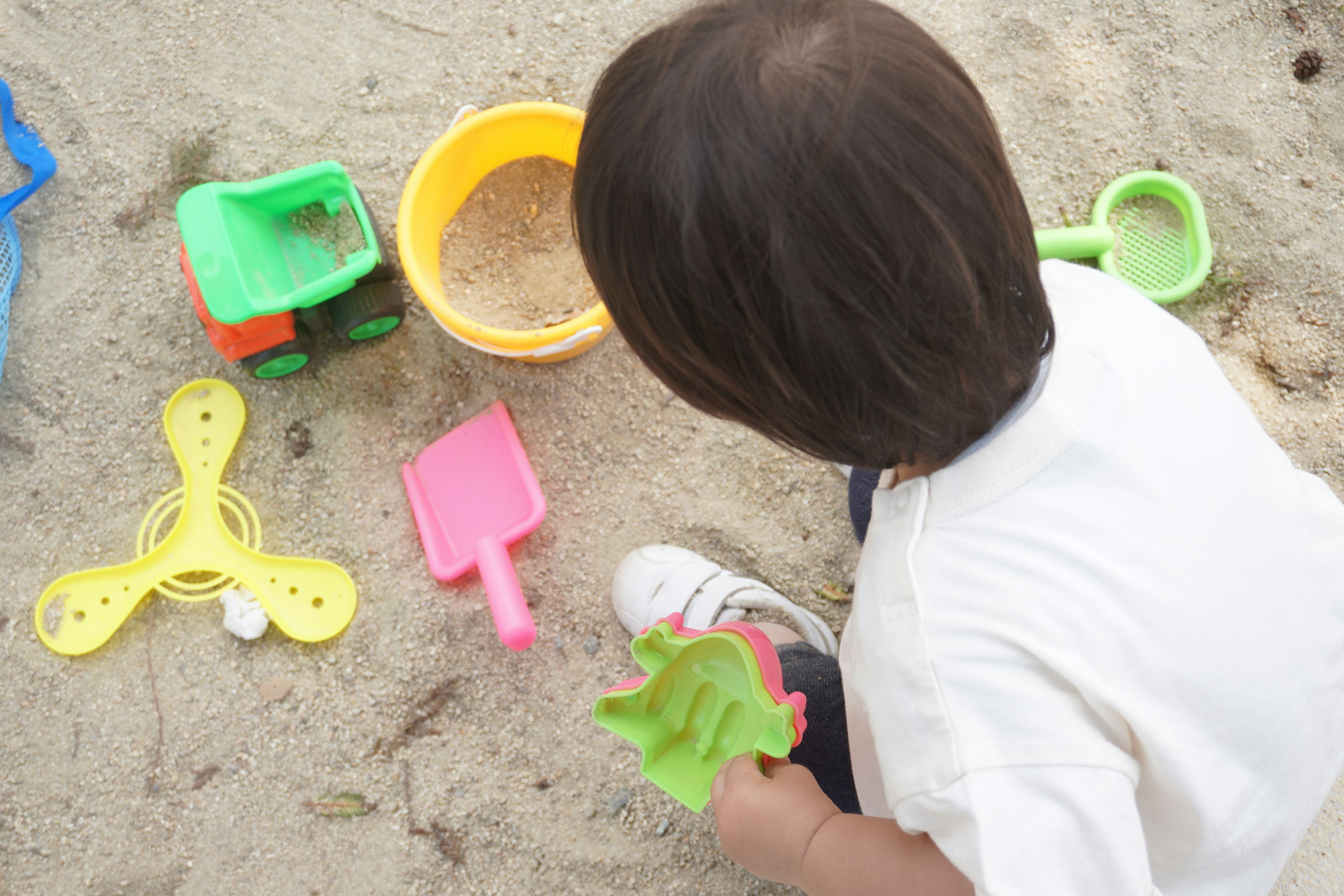 Kind spielt im Sandkasten umgeben von bunten Sandspielzeugen