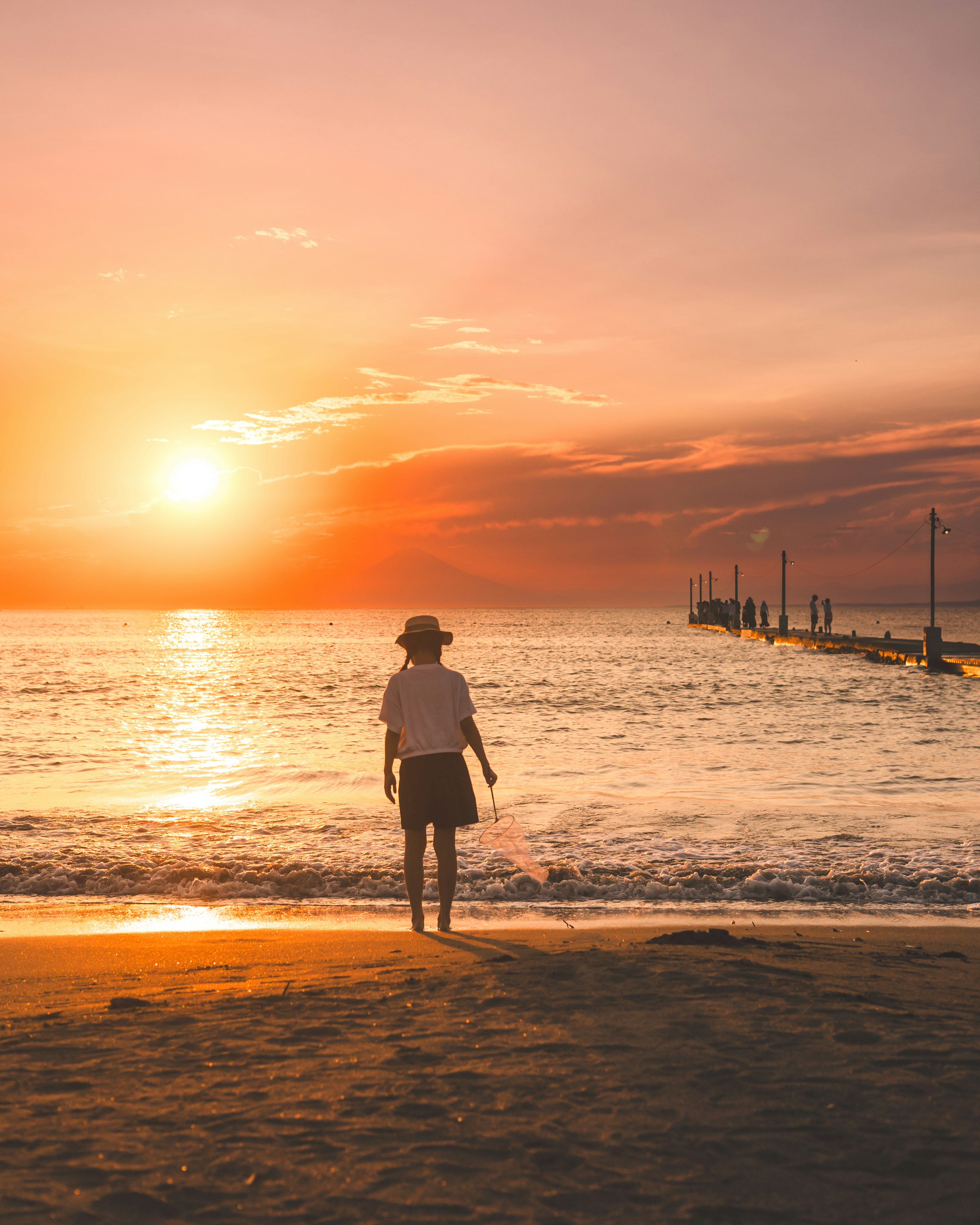 Silhouette d'une personne se tenant sur la plage avec un coucher de soleil en arrière-plan