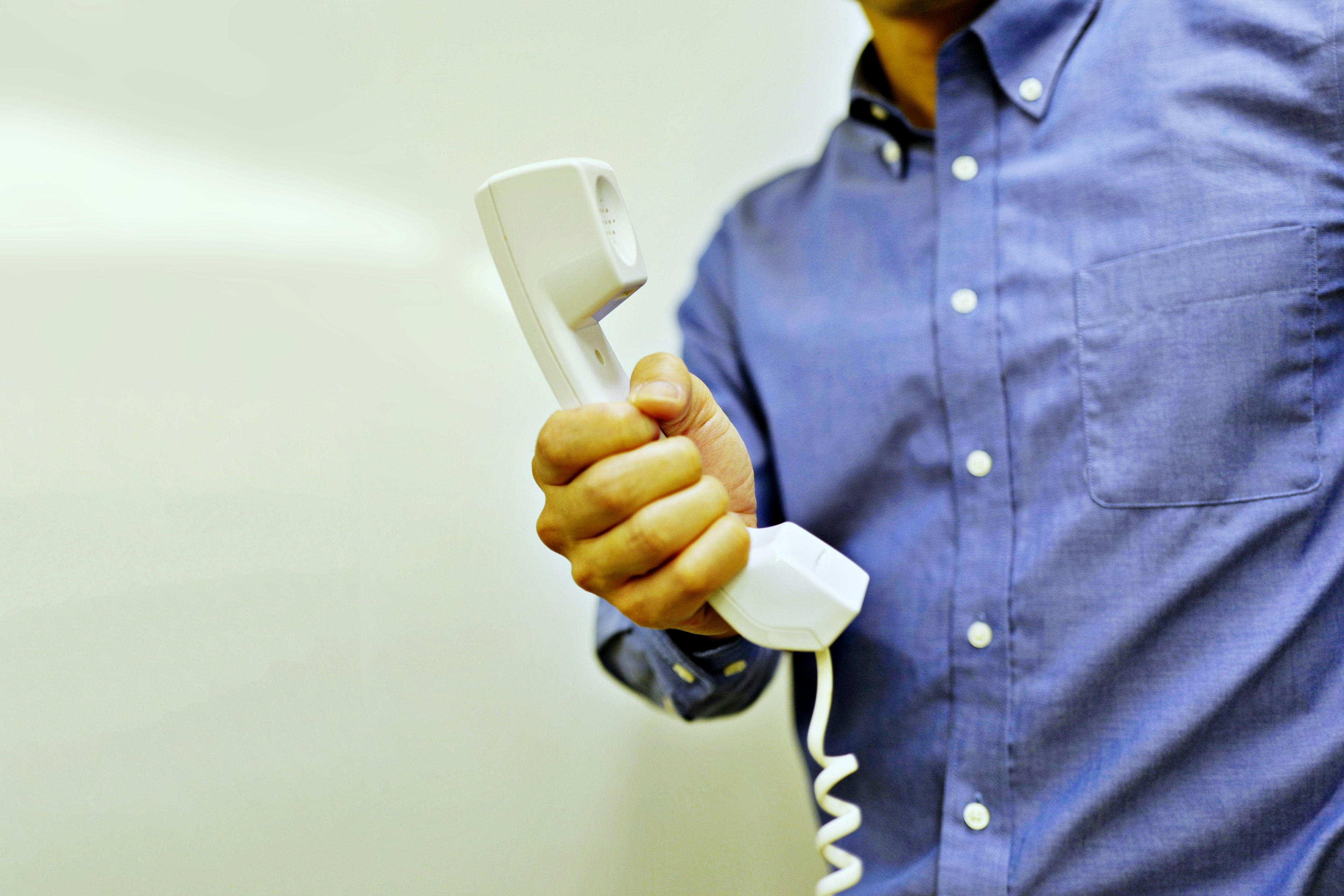 Primo piano della mano di un uomo che tiene un ricevitore telefonico bianco