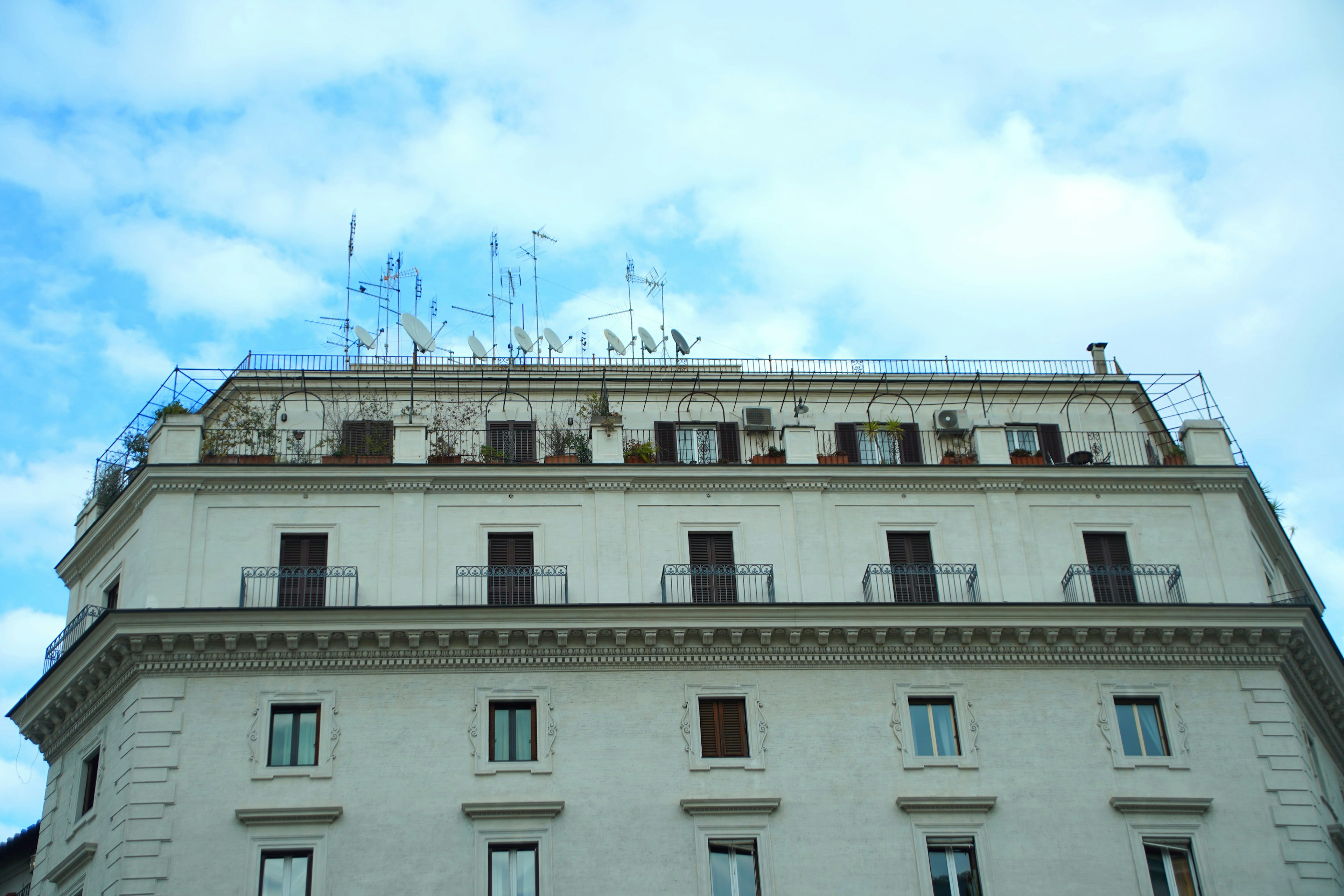 Upper section of a white building under a blue sky with rooftop antennas