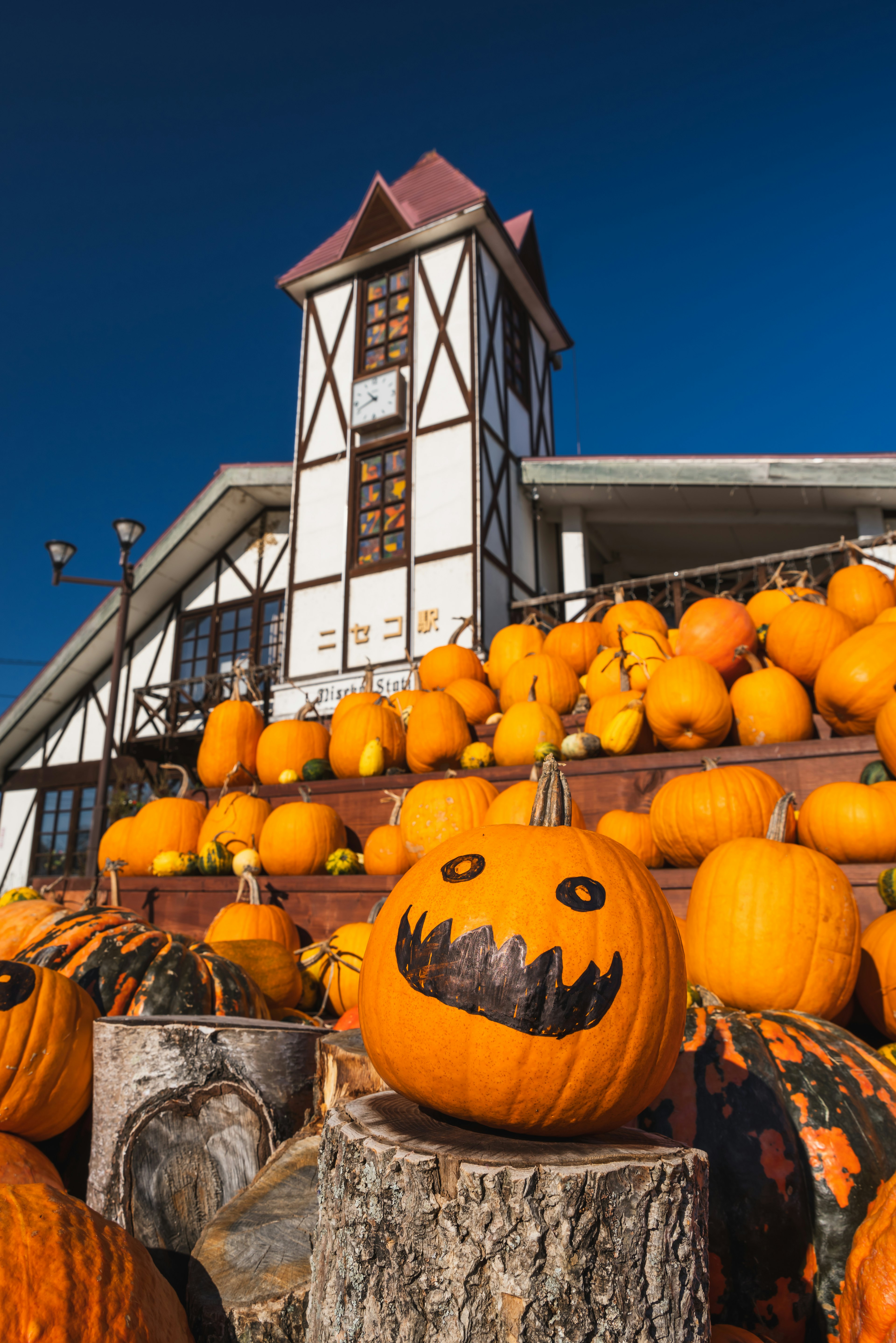 A landscape with stacked orange pumpkins and a building featuring a tower in the background