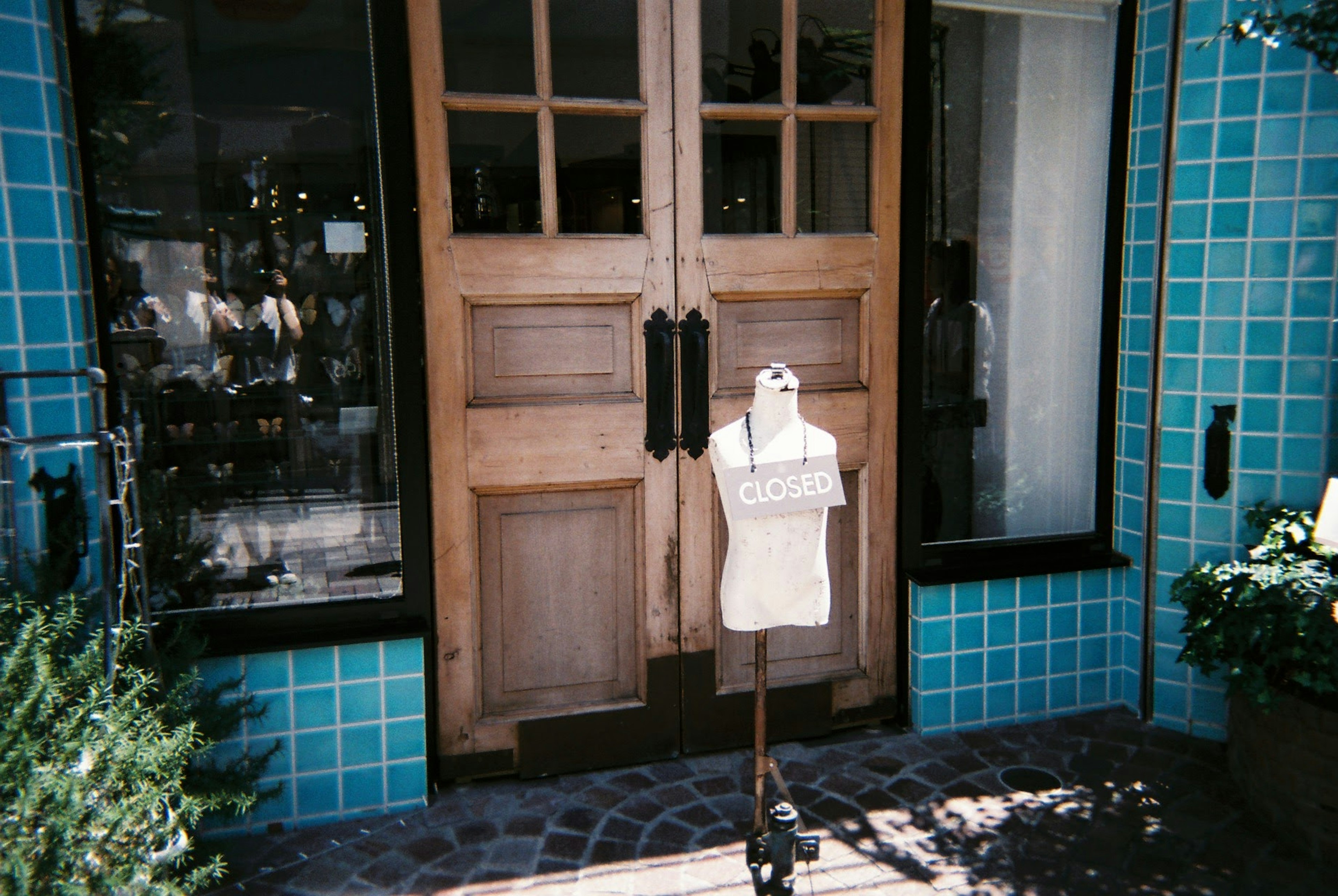 Un mannequin se tient devant un magasin avec des portes en bois et un extérieur carrelé bleu