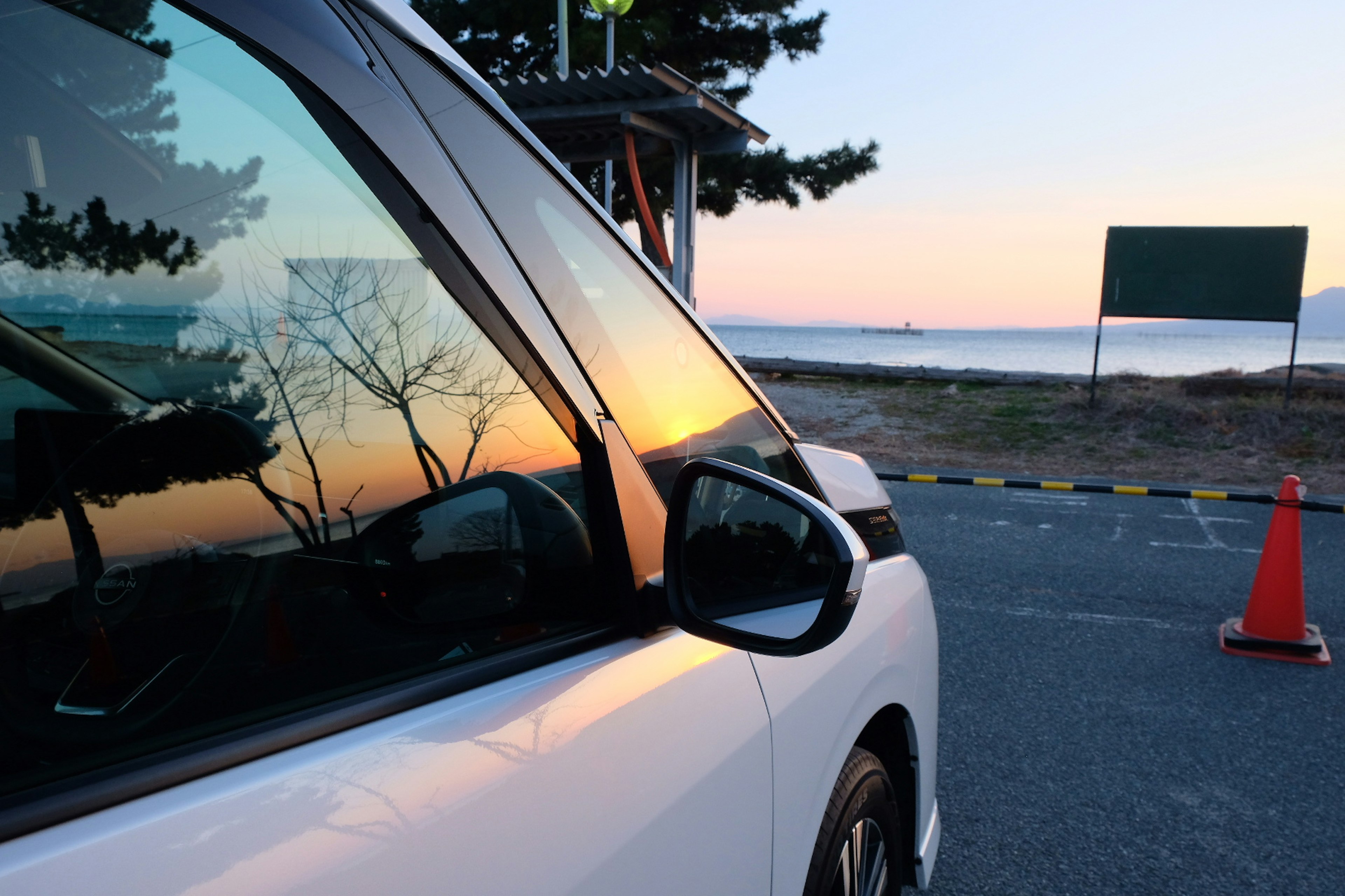 Vista laterale di un'auto bianca che riflette i colori del tramonto