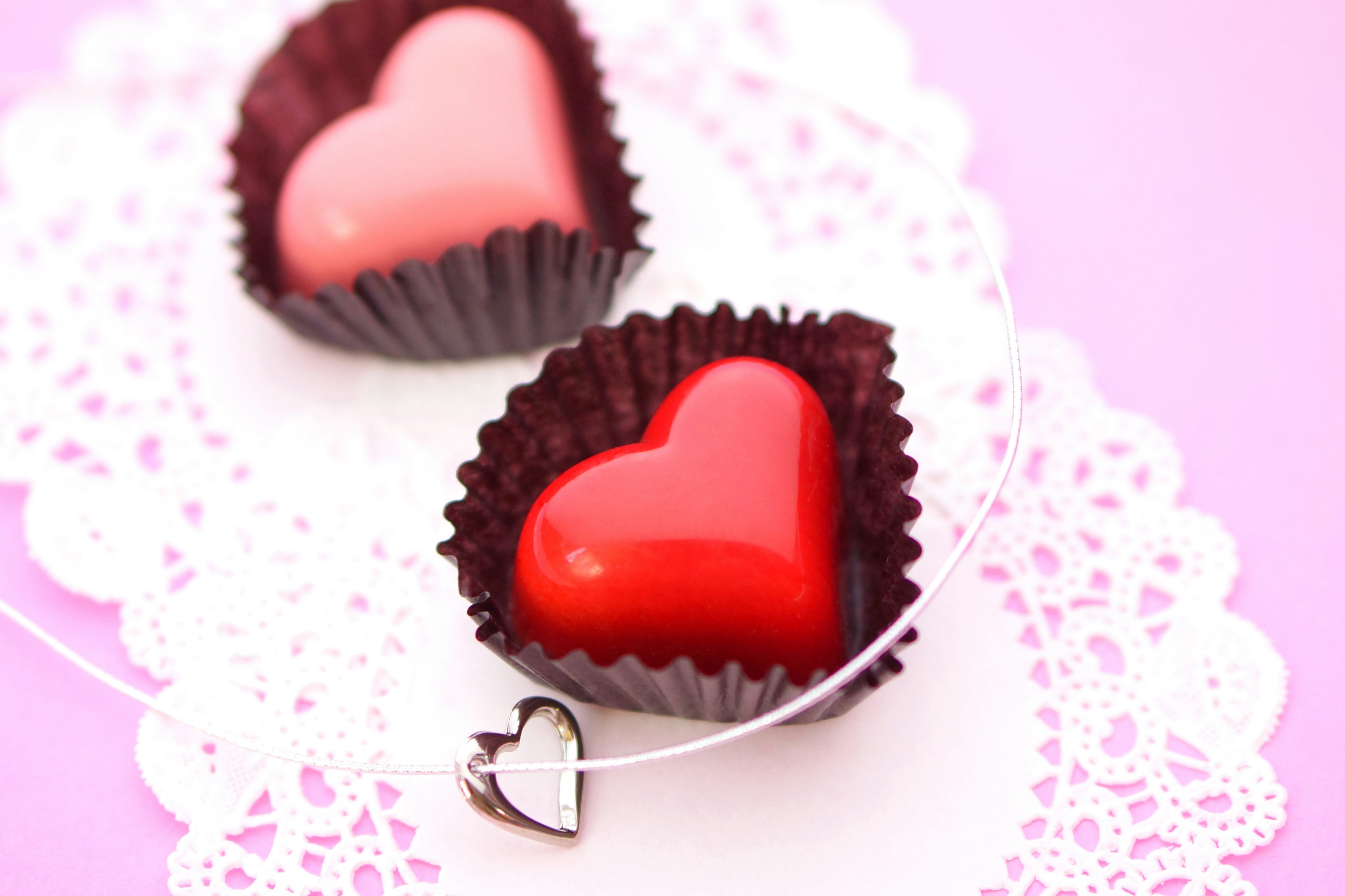 Chocolats en forme de cœur sur un fond rose placés sur une assiette en dentelle blanche