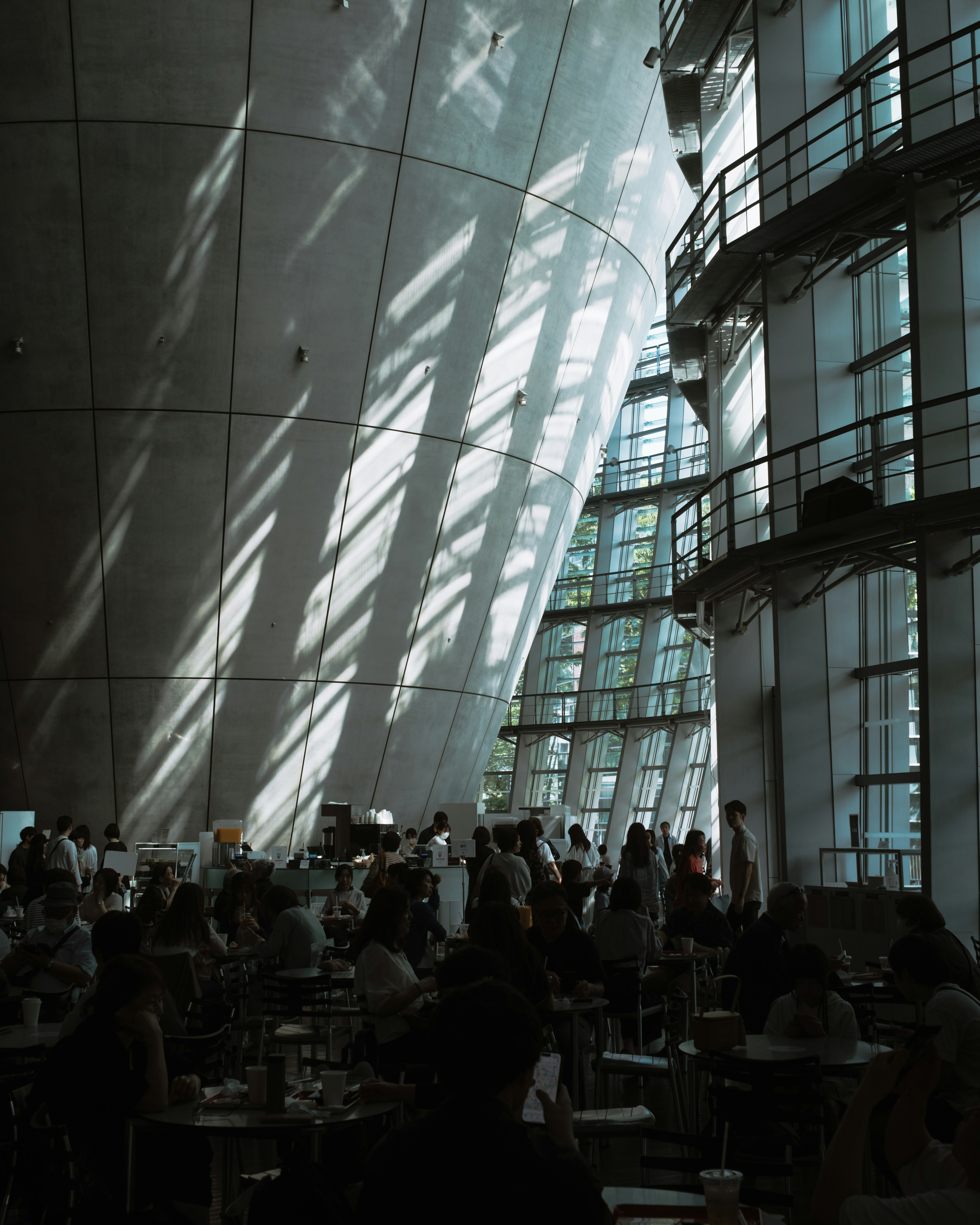 Modernes Innere eines Gebäudes mit Licht, das durch große Fenster strömt Menschen versammelt in einem Cafébereich mit dramatischen Schatten