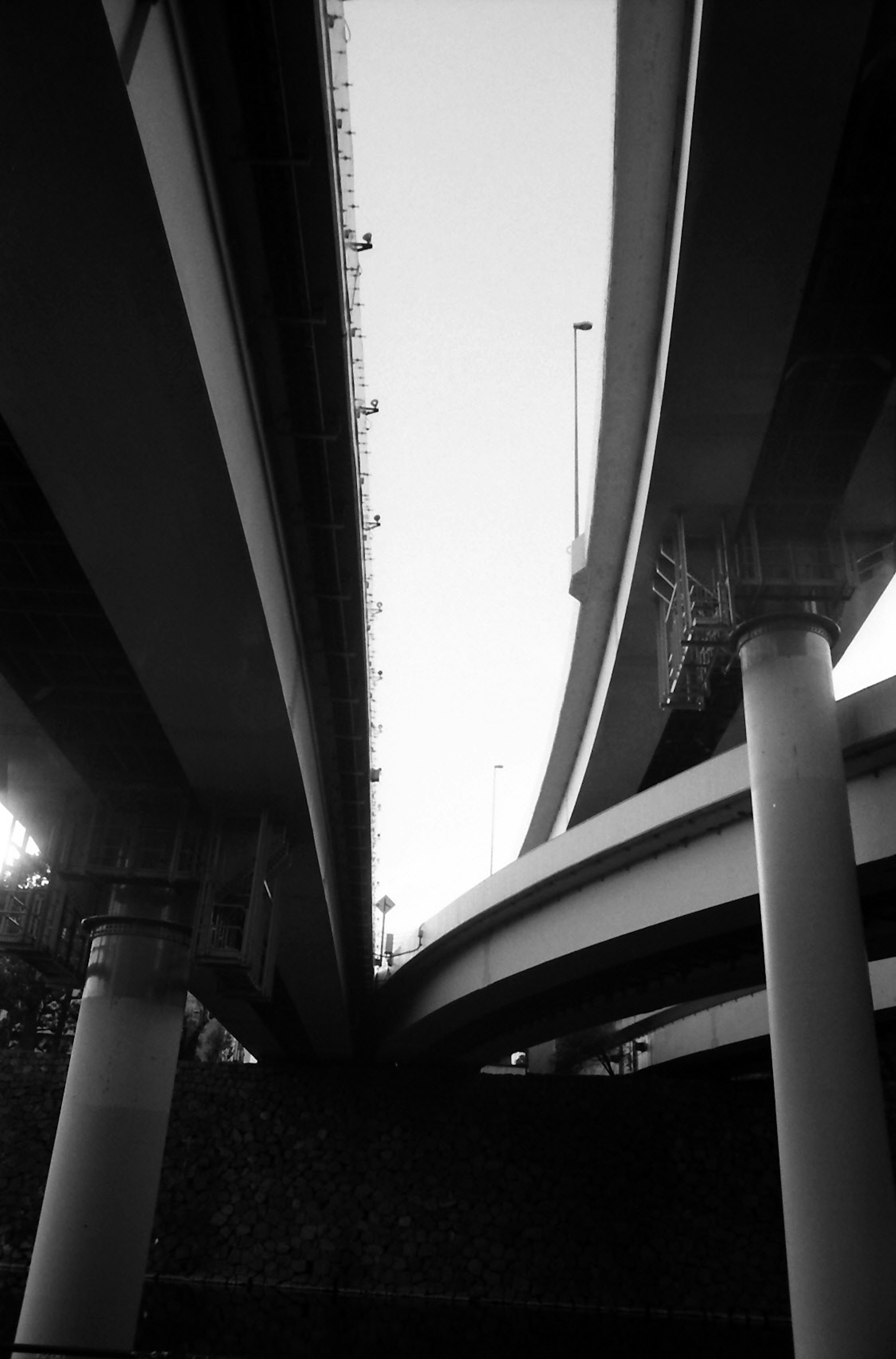 Schwarzweißfoto, das das Ineinandergreifen von Strukturen unter einer Autobahn festhält