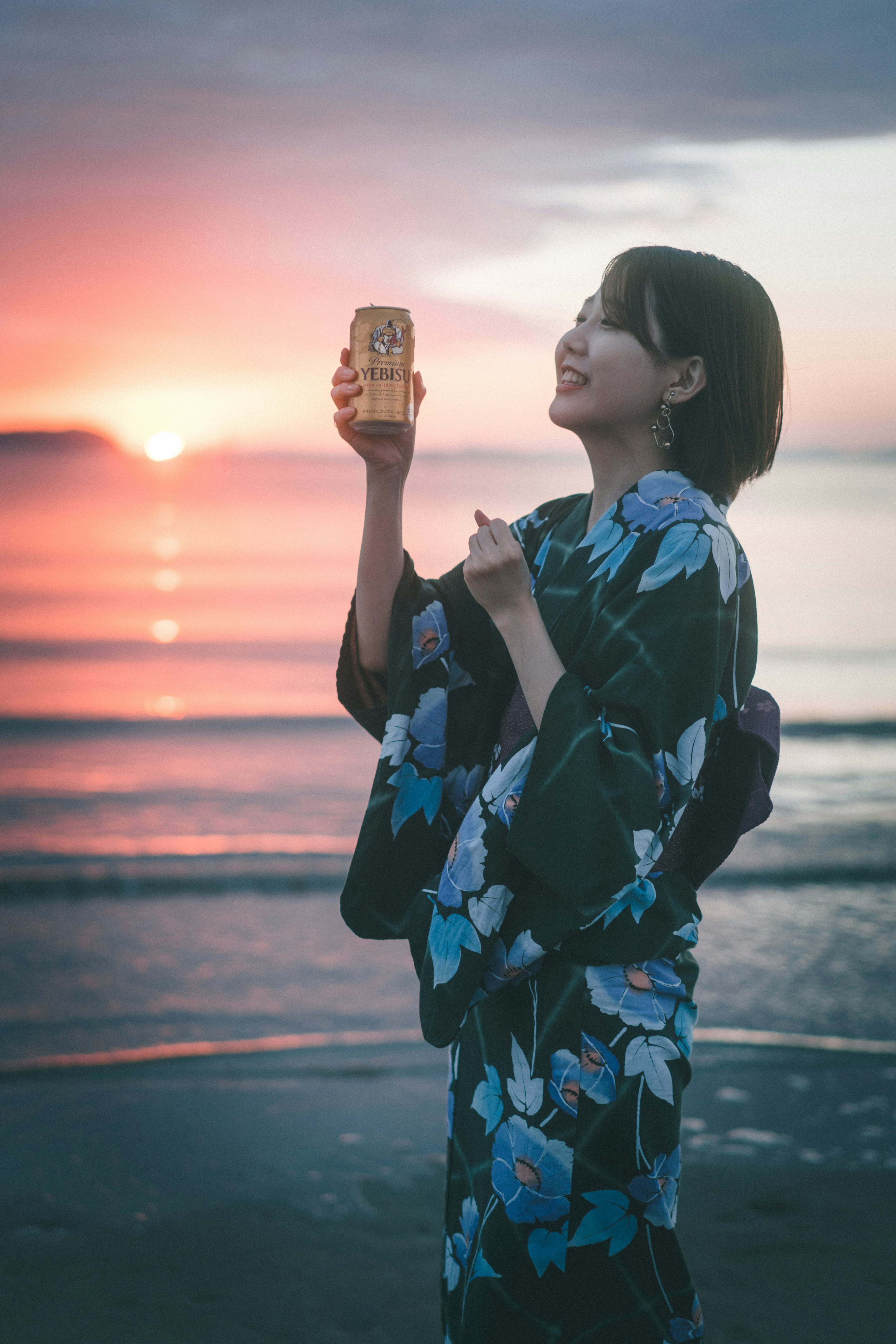 Eine Frau in einem japanischen Yukata lächelt, während sie etwas vor einem schönen Sonnenuntergang hält