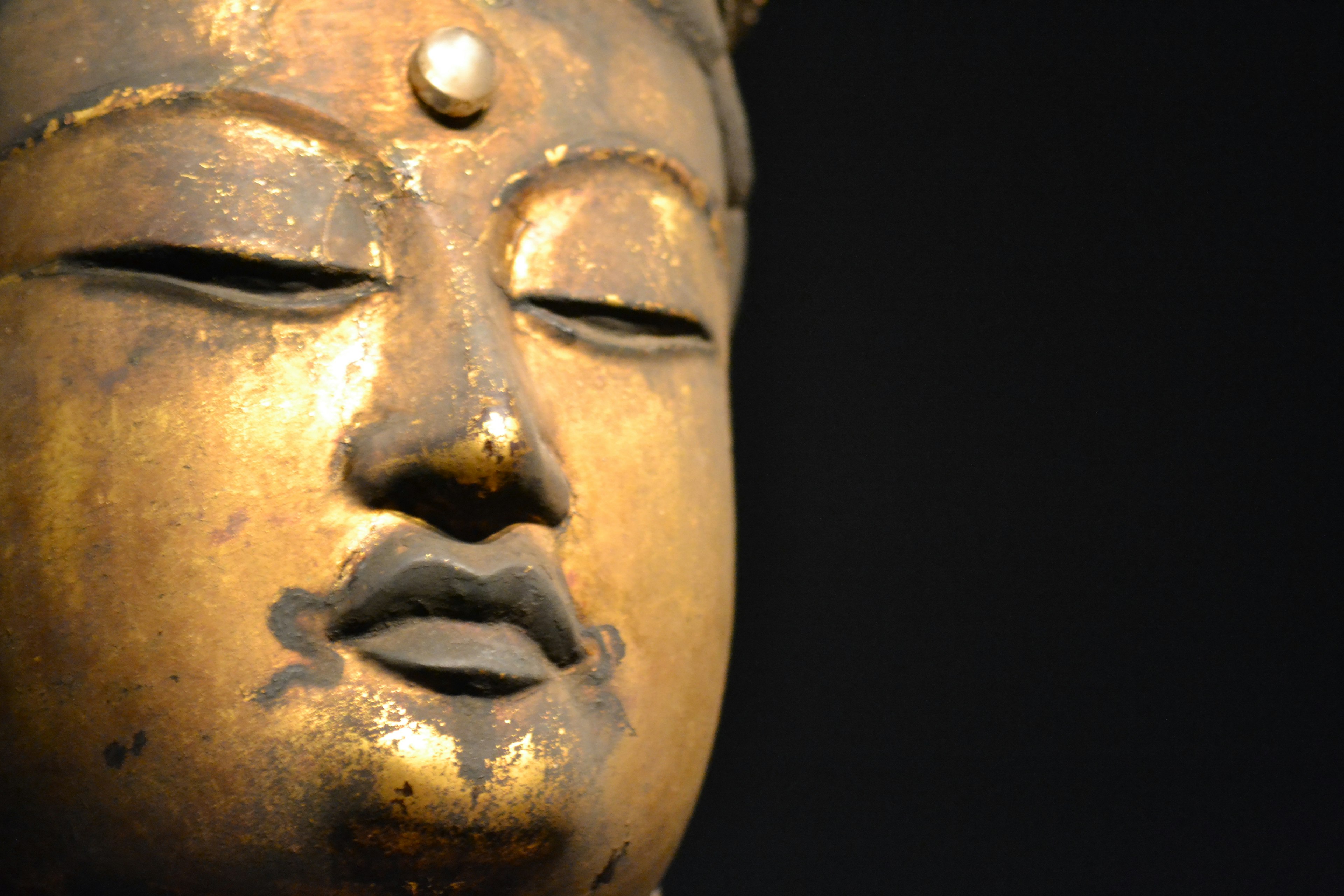 Primo piano di un volto di statua di Buddha dorato con espressione serena e dettagli intricati su sfondo nero