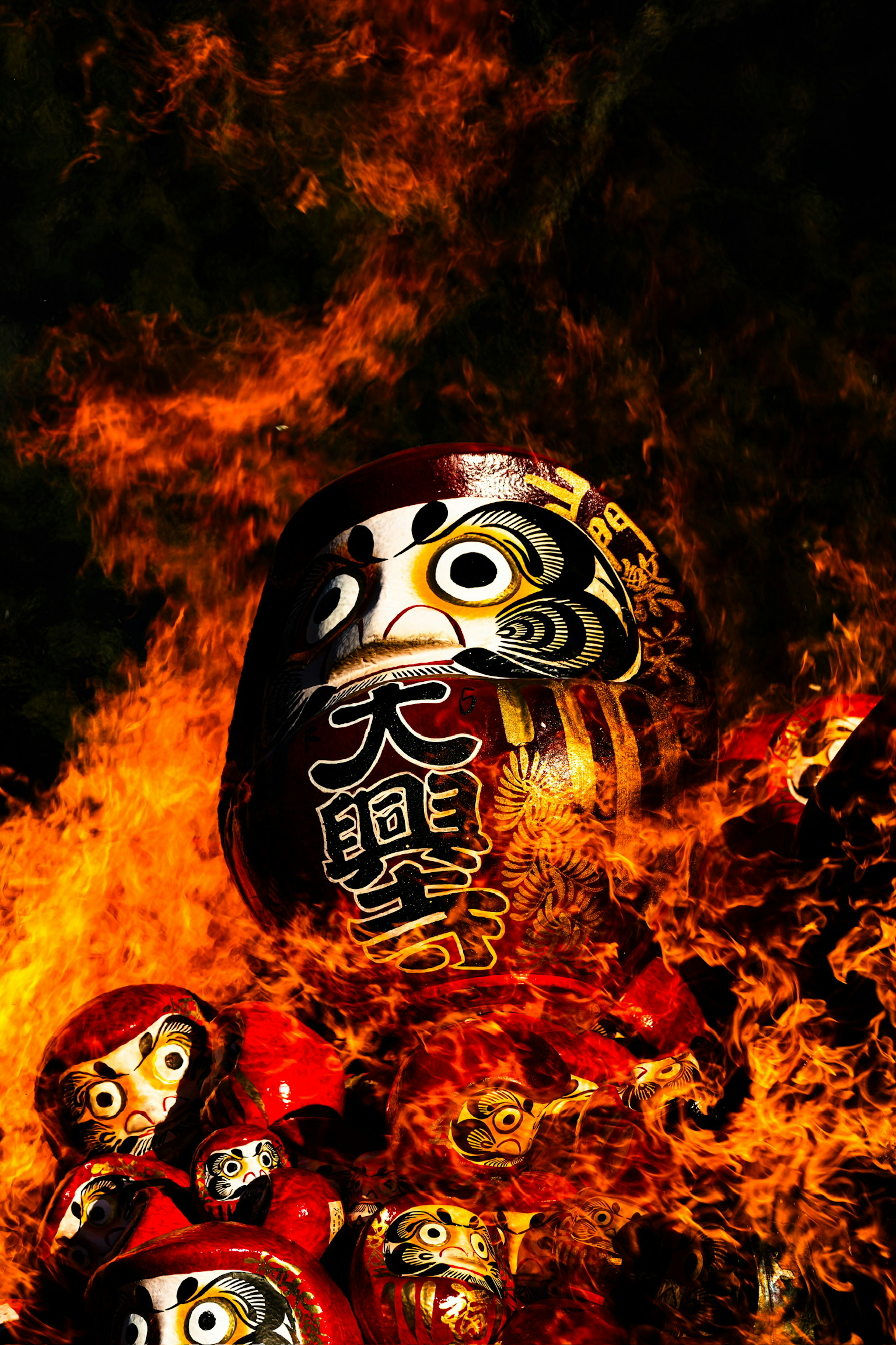 Gruppe von Daruma-Puppen umgeben von Flammen mit einem großen Daruma-Gesicht