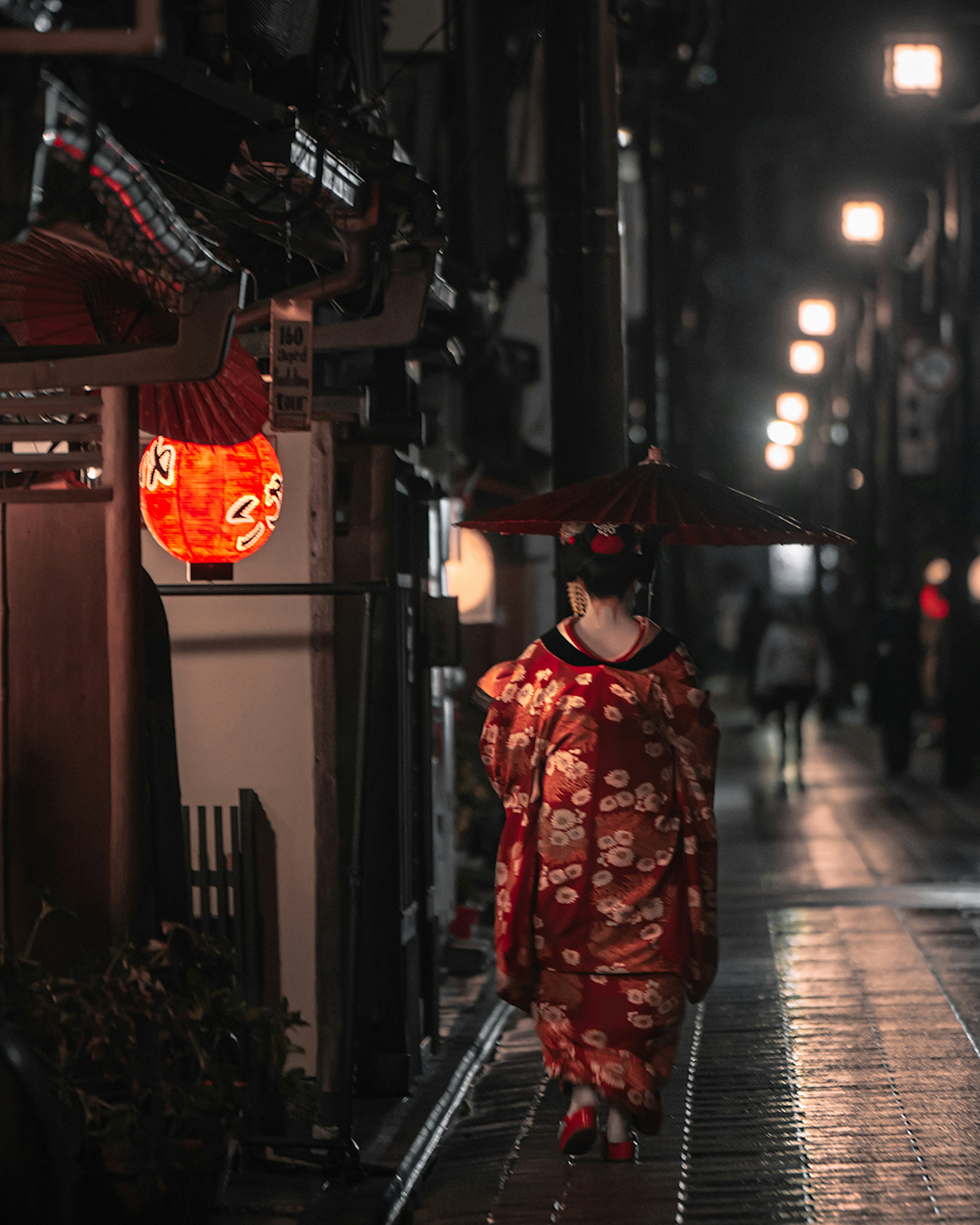 Mujer en kimono rojo caminando en una calle nocturna con faroles