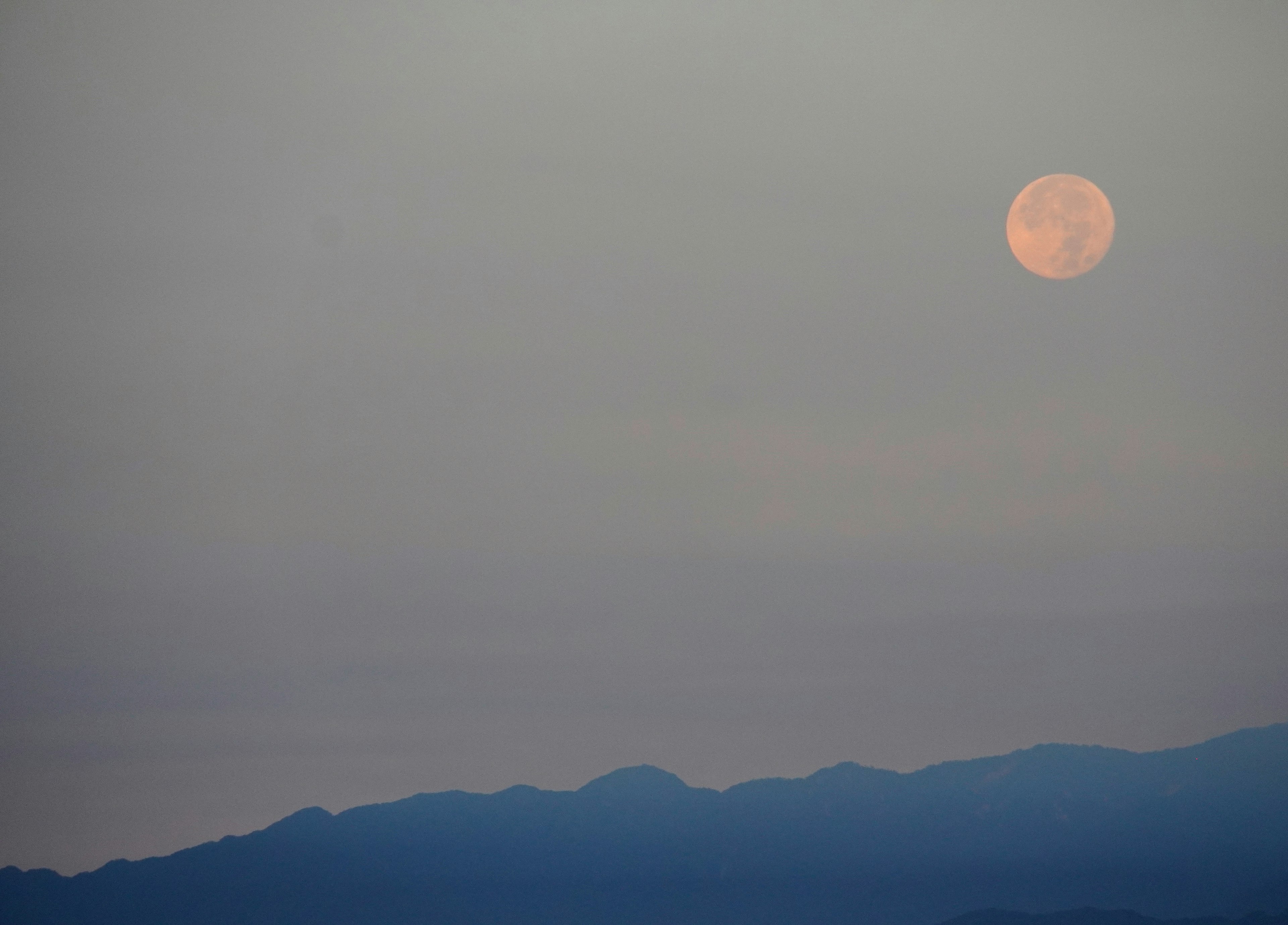 Luna arancione grande che sorge su una catena montuosa nebbiosa