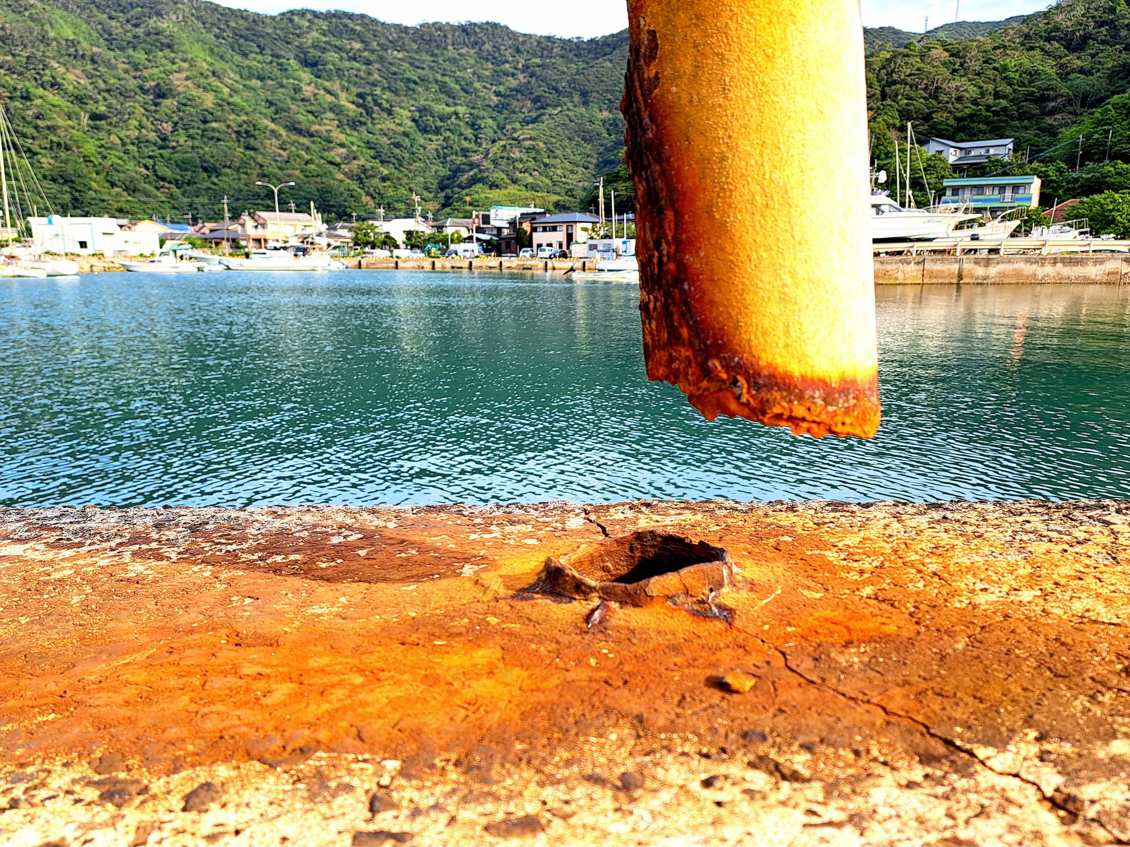 Close-up of a rusted pillar and damaged ground near the sea