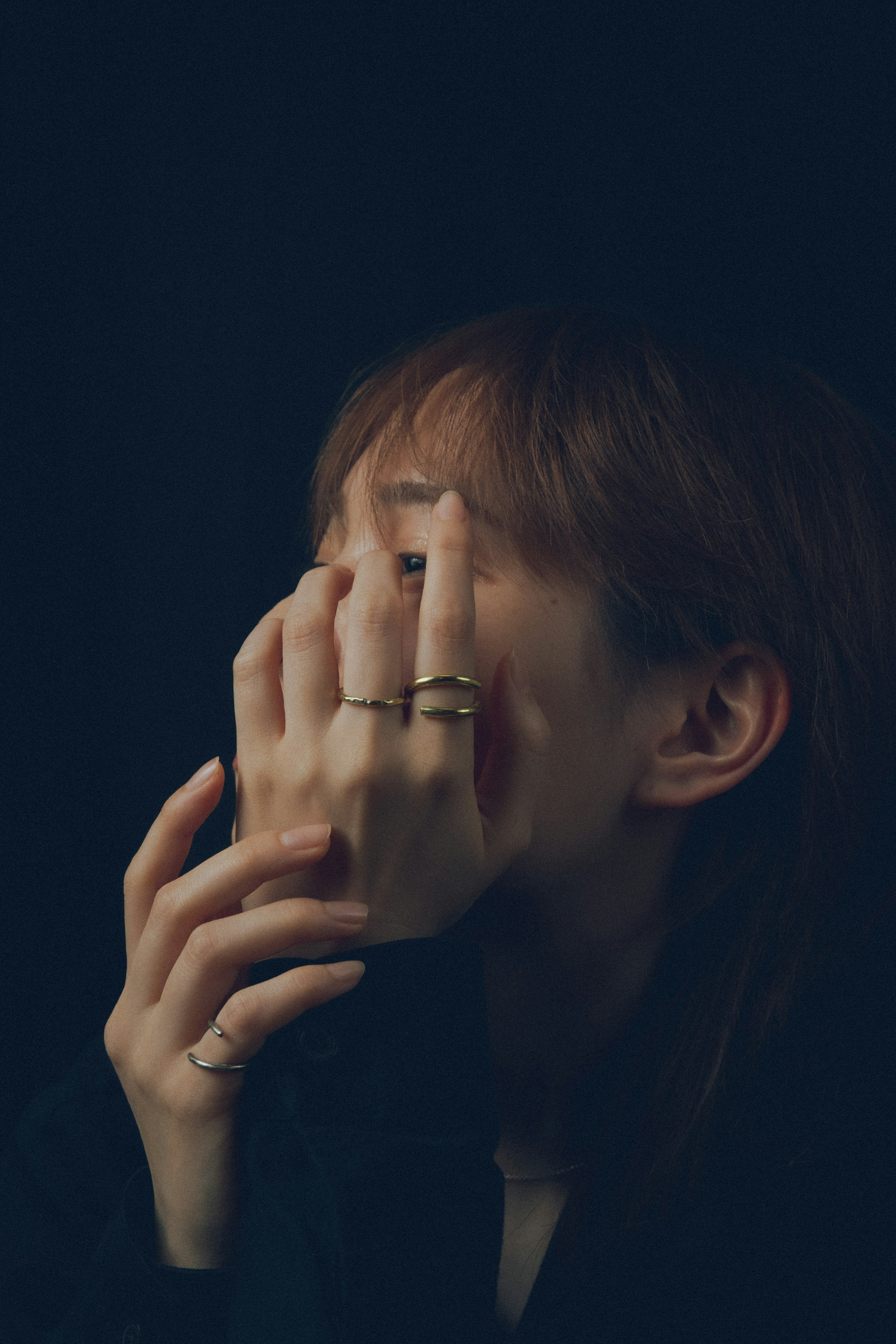 Retrato de una mujer cubriendo su rostro con las manos contra un fondo oscuro