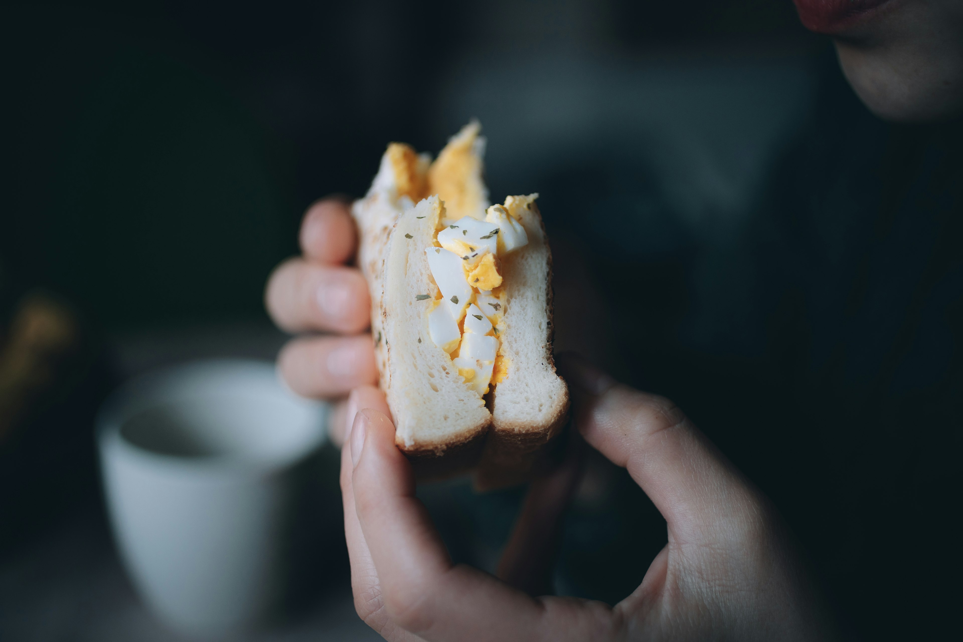 Close-up of a sandwich being held with visible layers of egg and bread