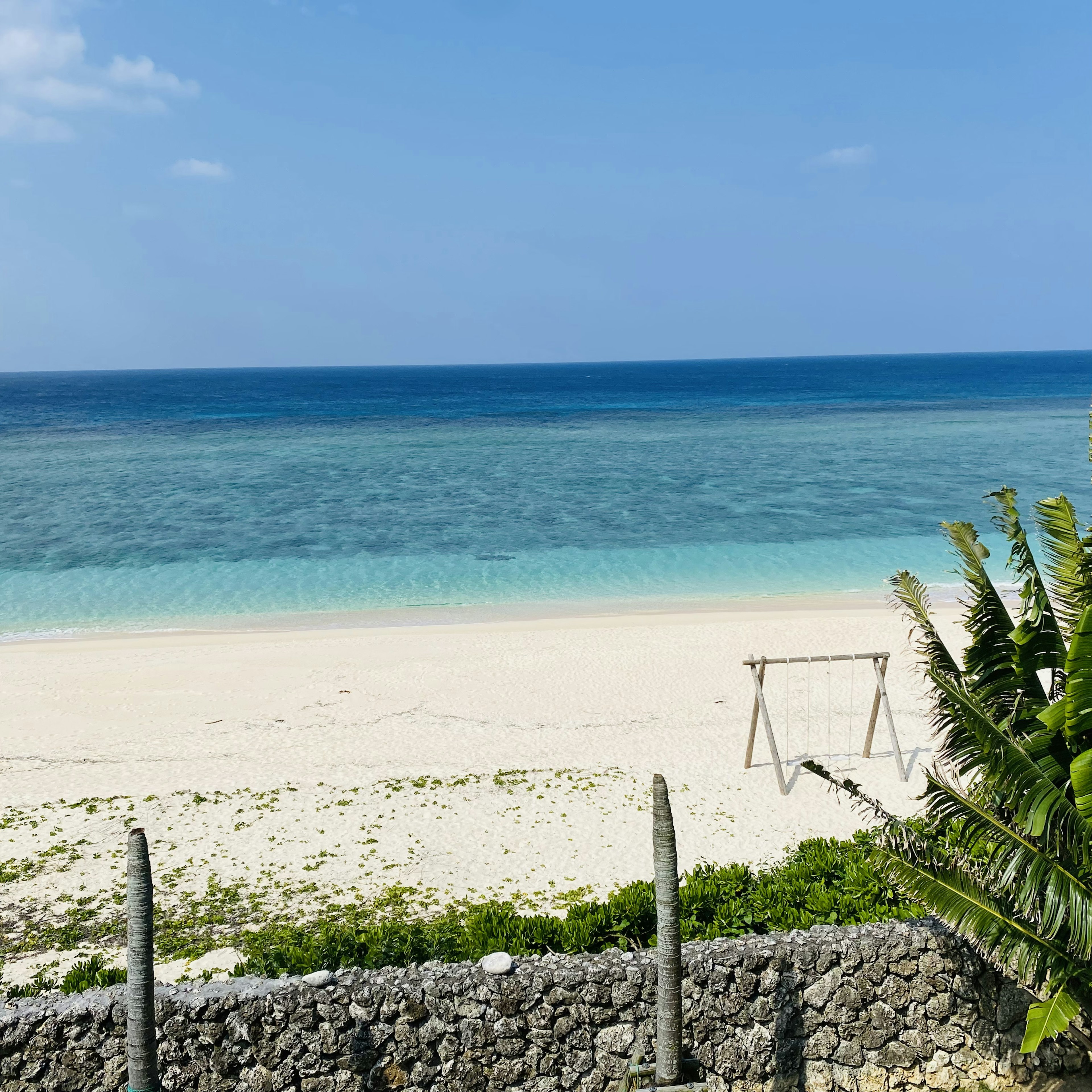 Vista escénica de una playa con agua azul y arena blanca con un columpio