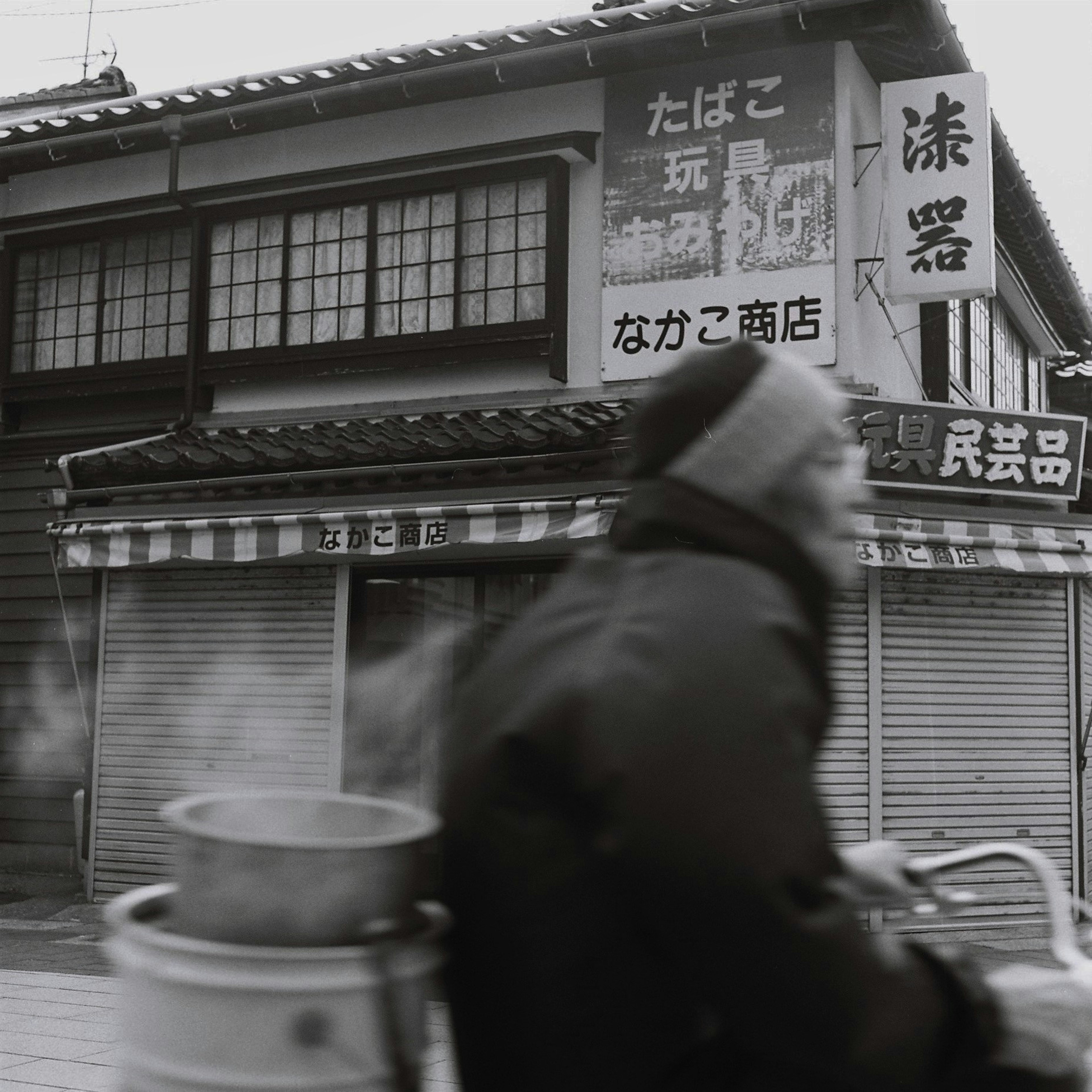 Una persona empujando una bicicleta en una escena de calle en blanco y negro con letreros de tienda