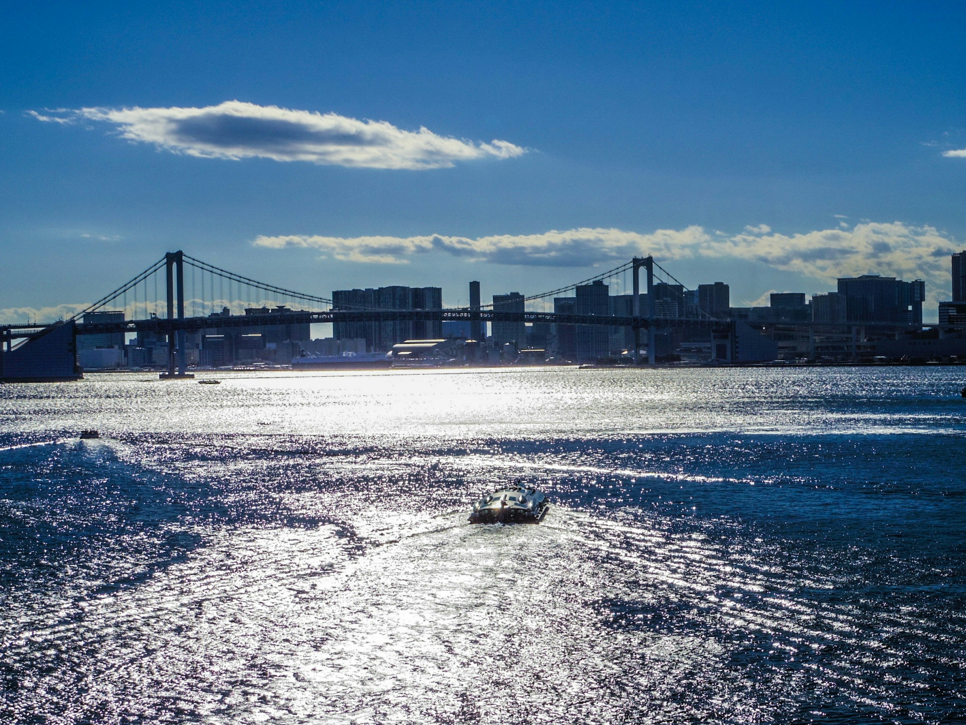 Un bote en agua brillante con un horizonte y un puente bajo un cielo azul