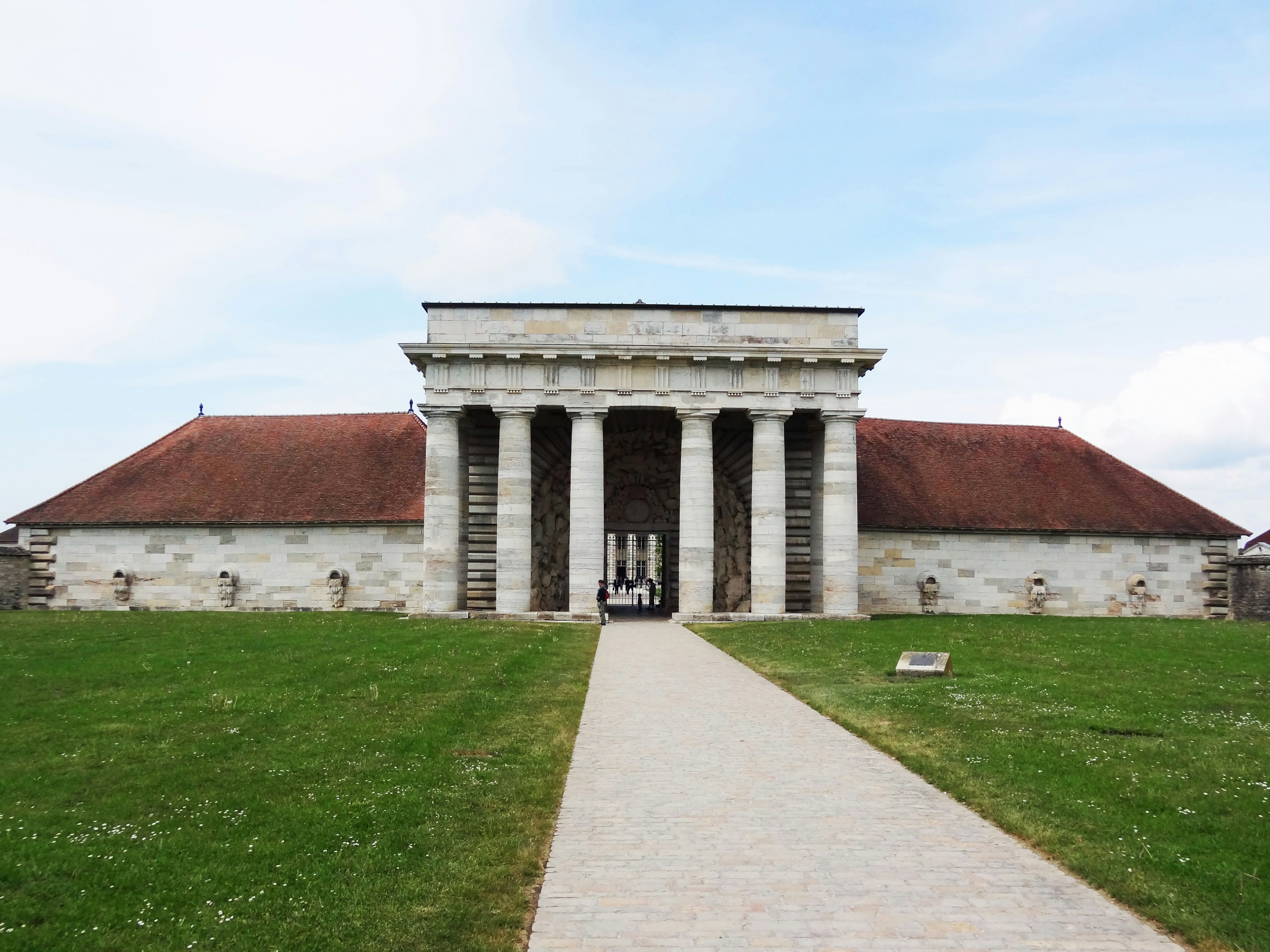 Extérieur d'un bâtiment ancien avec des colonnes et un toit rouge distinctif entouré d'herbe verte