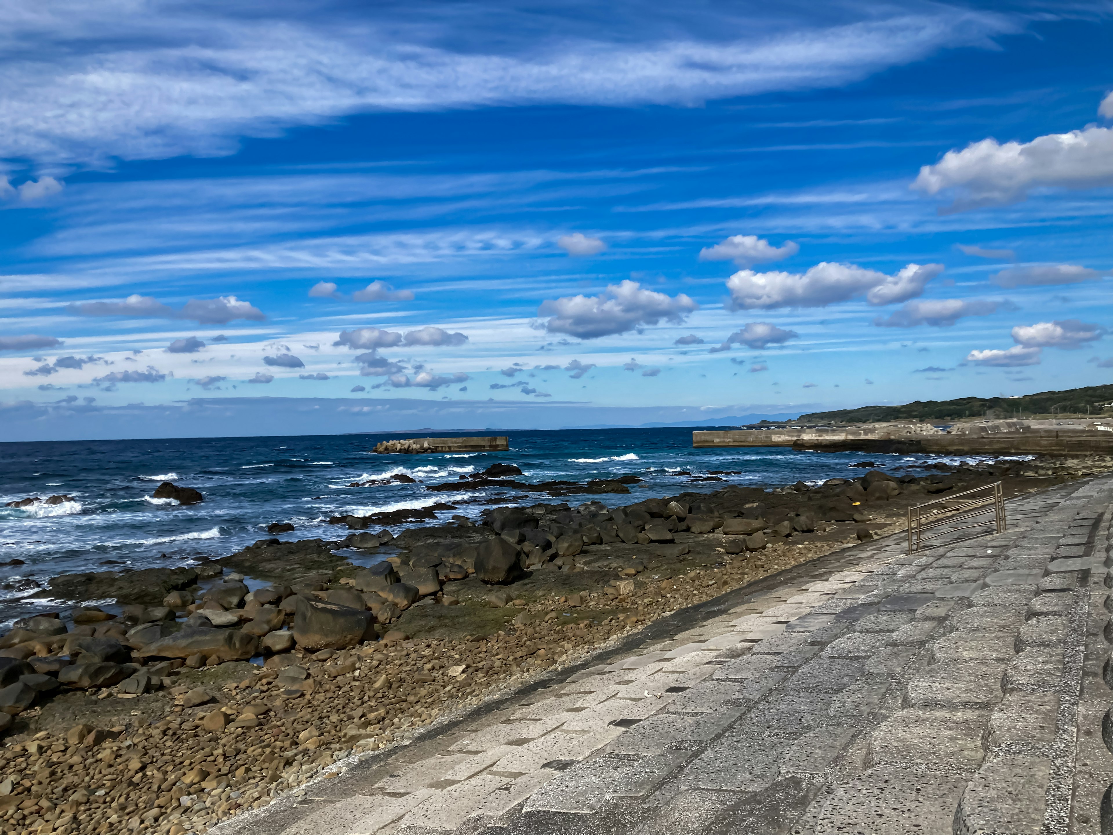 青い空と白い雲が広がる海岸の風景 岩だらけの海岸線と石畳の道が見える