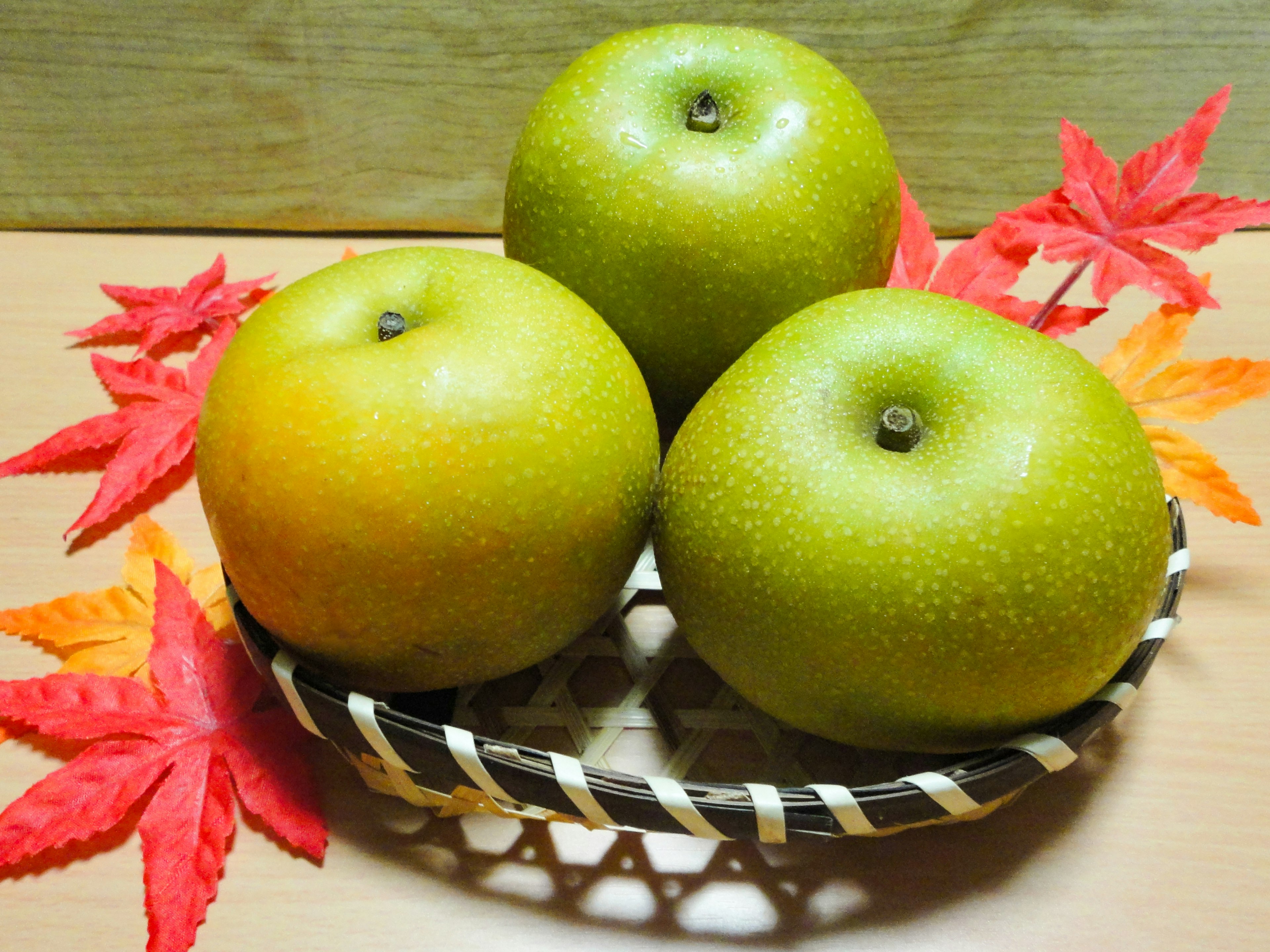 Three green apples in a woven basket with autumn leaves