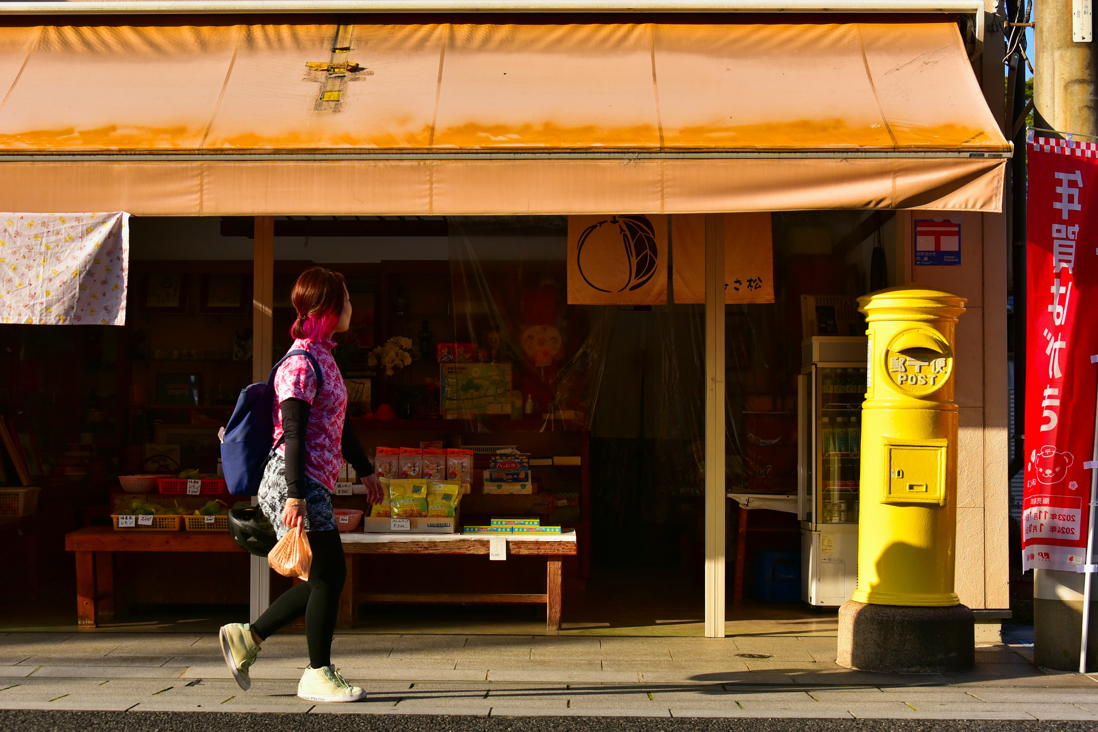 黄色い郵便ポストと古い店舗の前を歩く女性