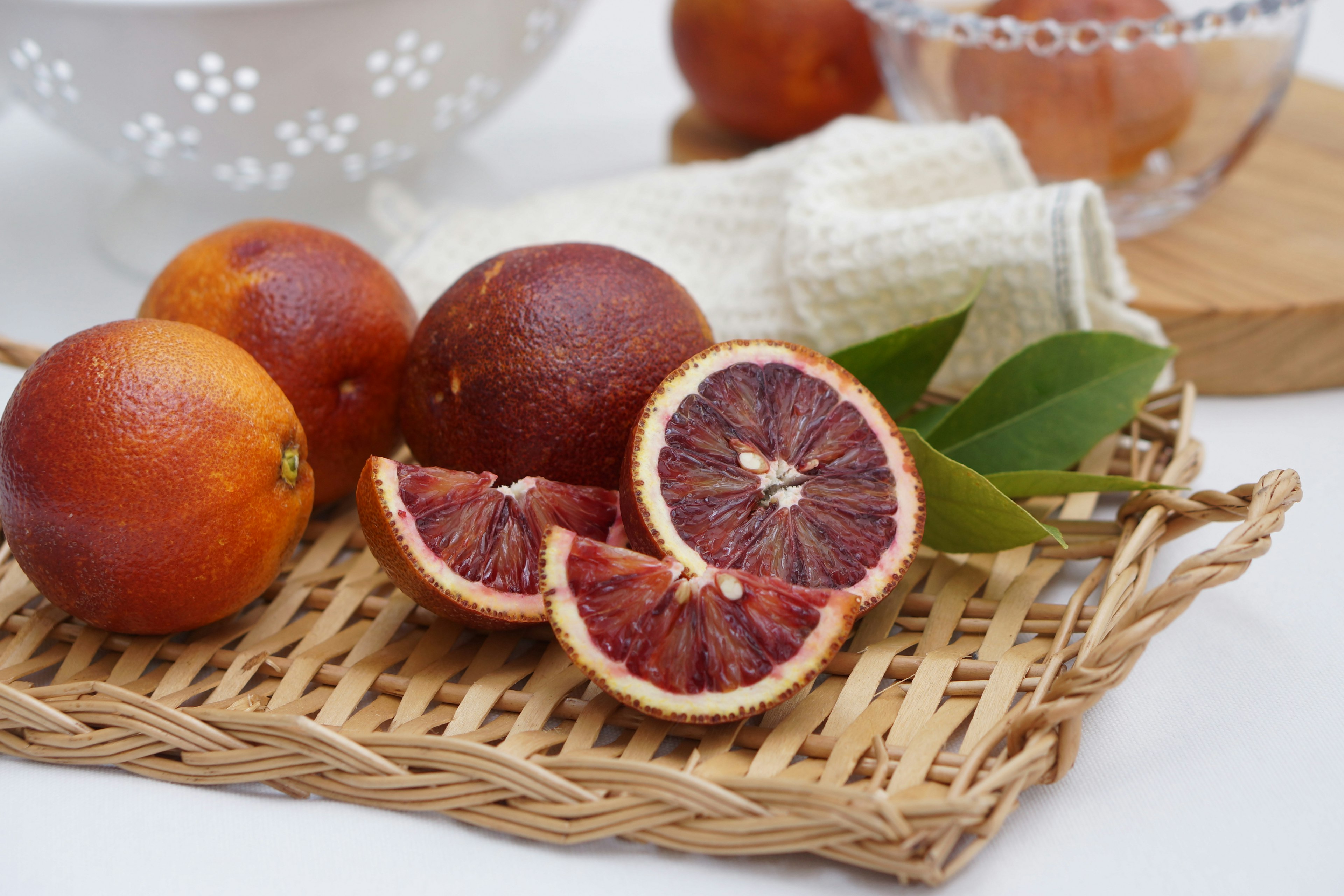 Blood oranges arranged in a basket with sliced blood orange and green leaves