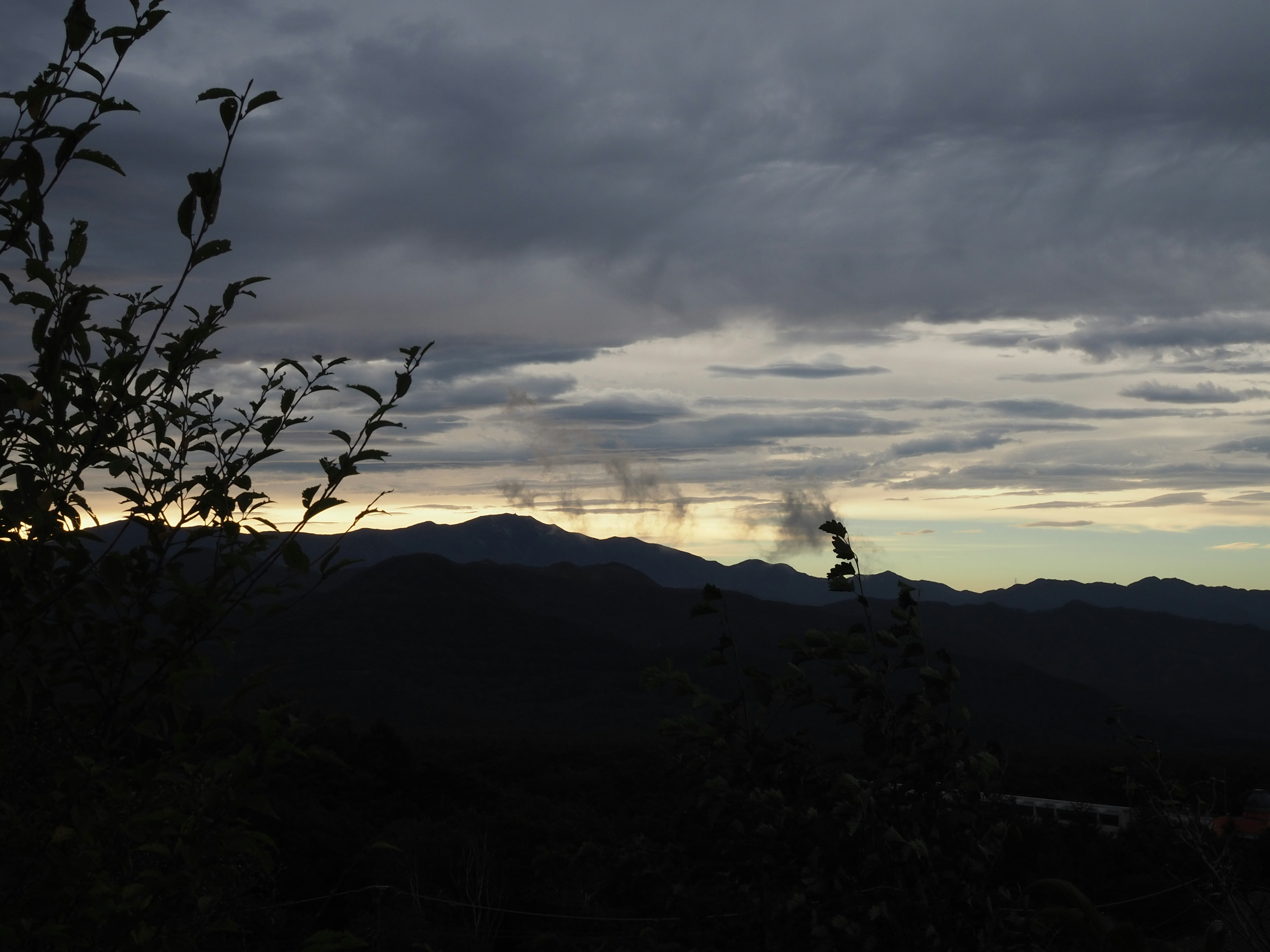 暗い雲に覆われた山のシルエットと薄明かりの空