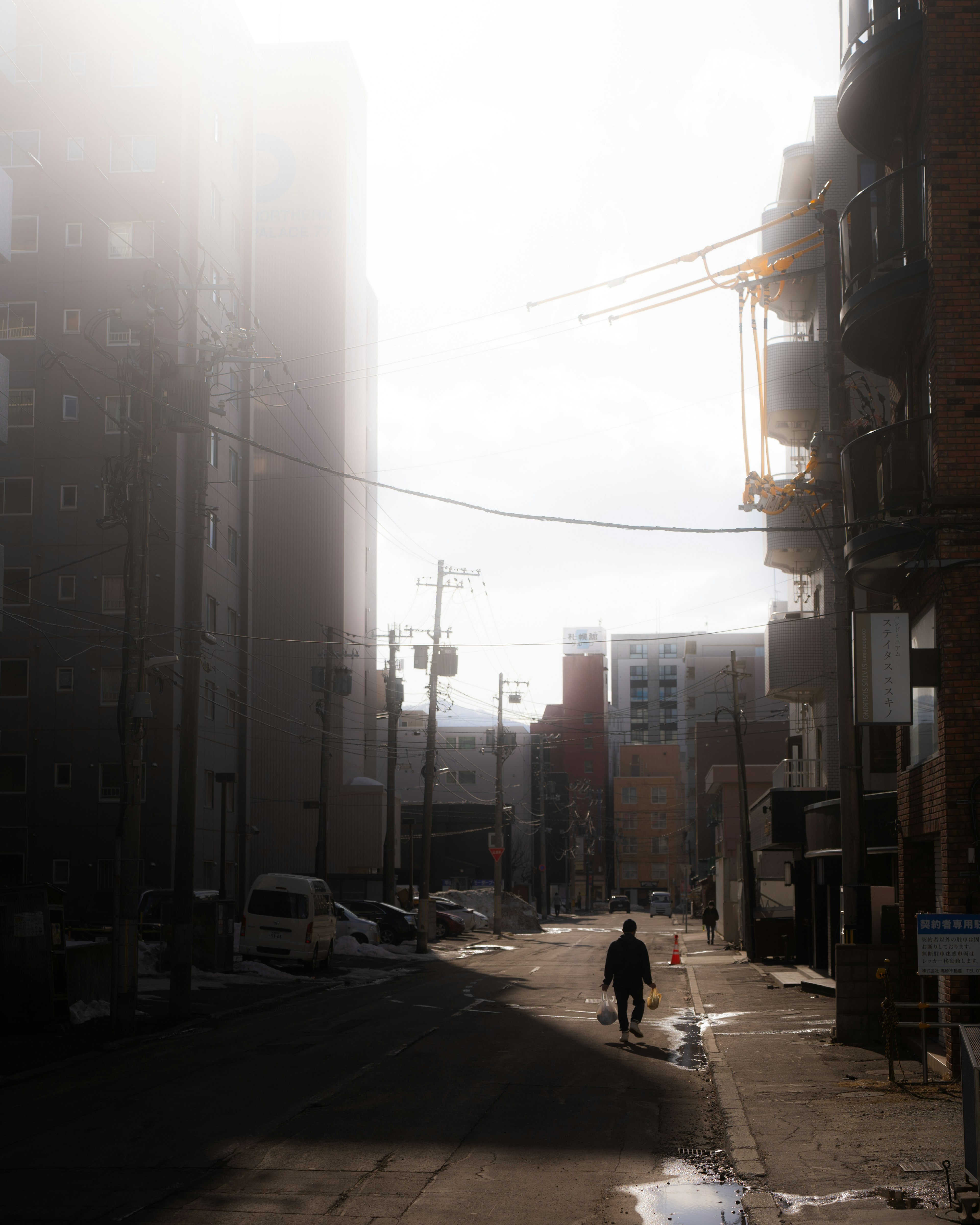 A person walking down a dimly lit street with buildings and a construction crane