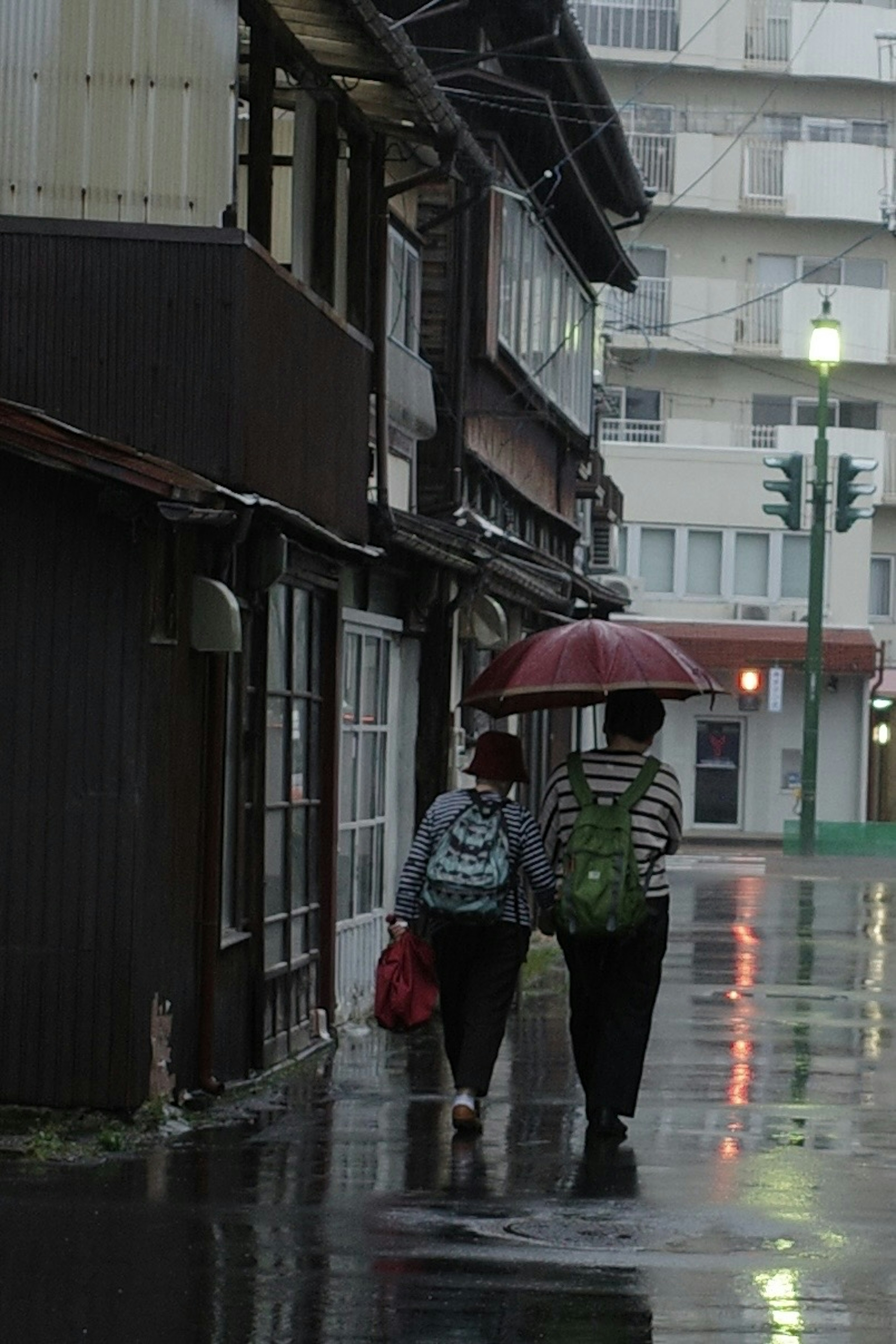 雨の中、傘をさして歩くカップルの姿が見える古い町並み