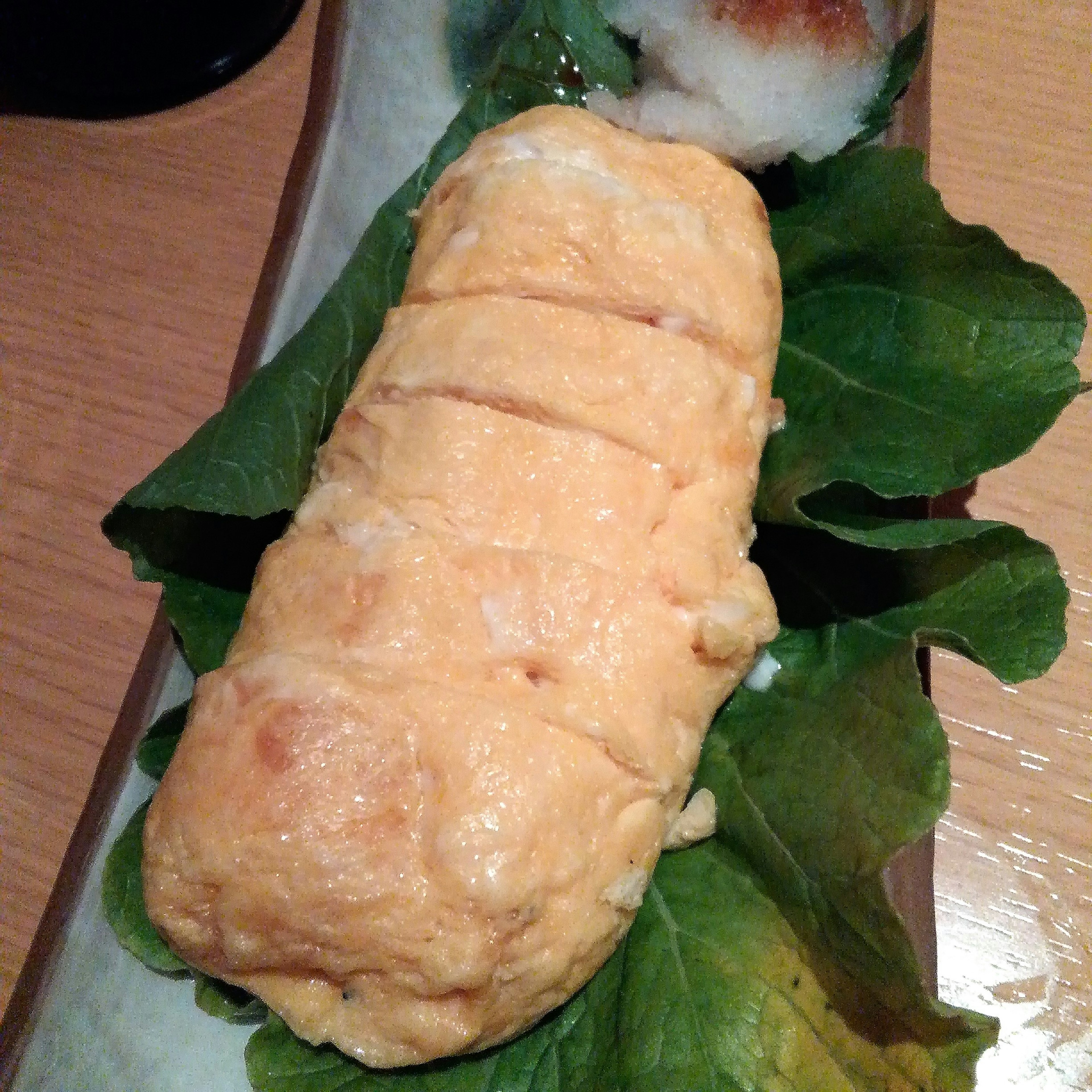 A Japanese omelette served on a leaf with sushi in the background