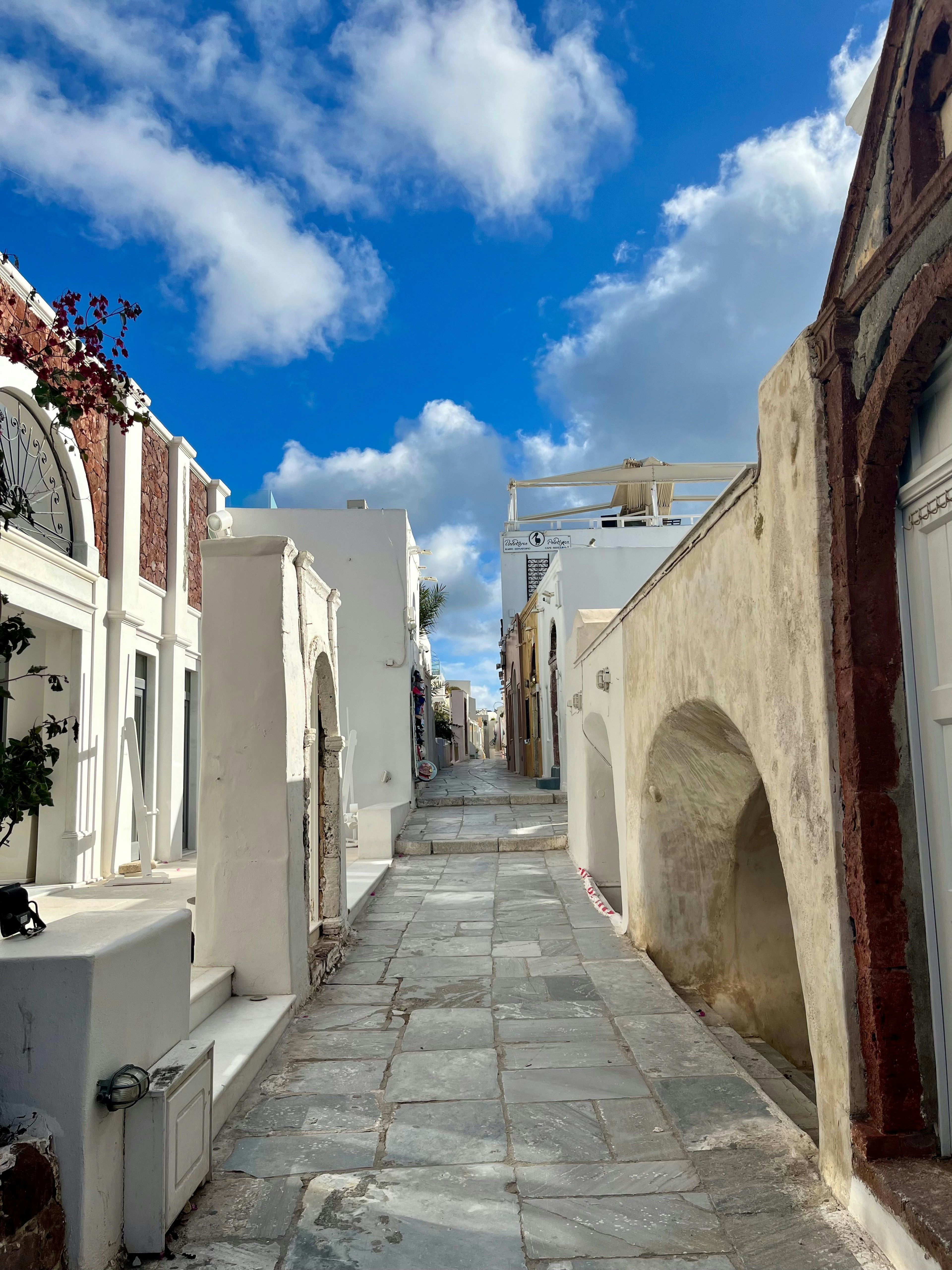 Narrow street in Santorini lined with white buildings and blue sky